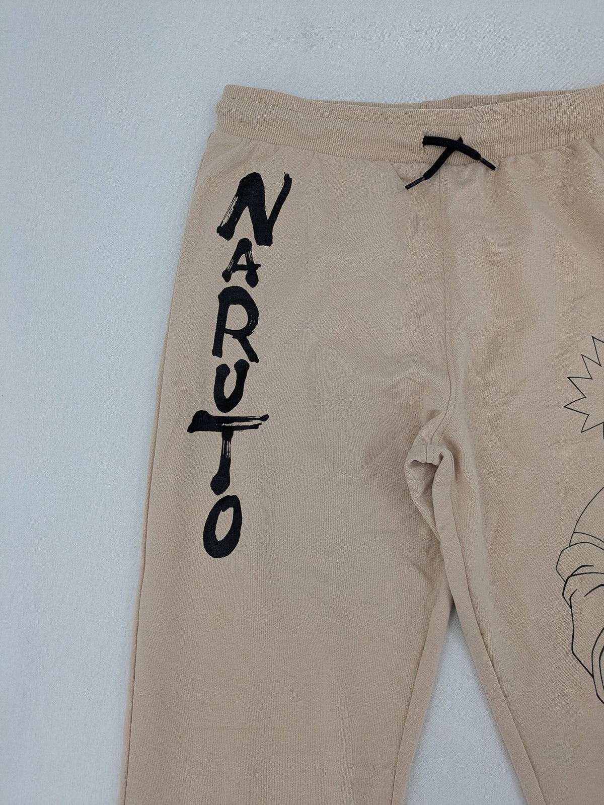 Naruto Shippuden beige joggers featuring Naruto Uzumaki graphic and logo print.