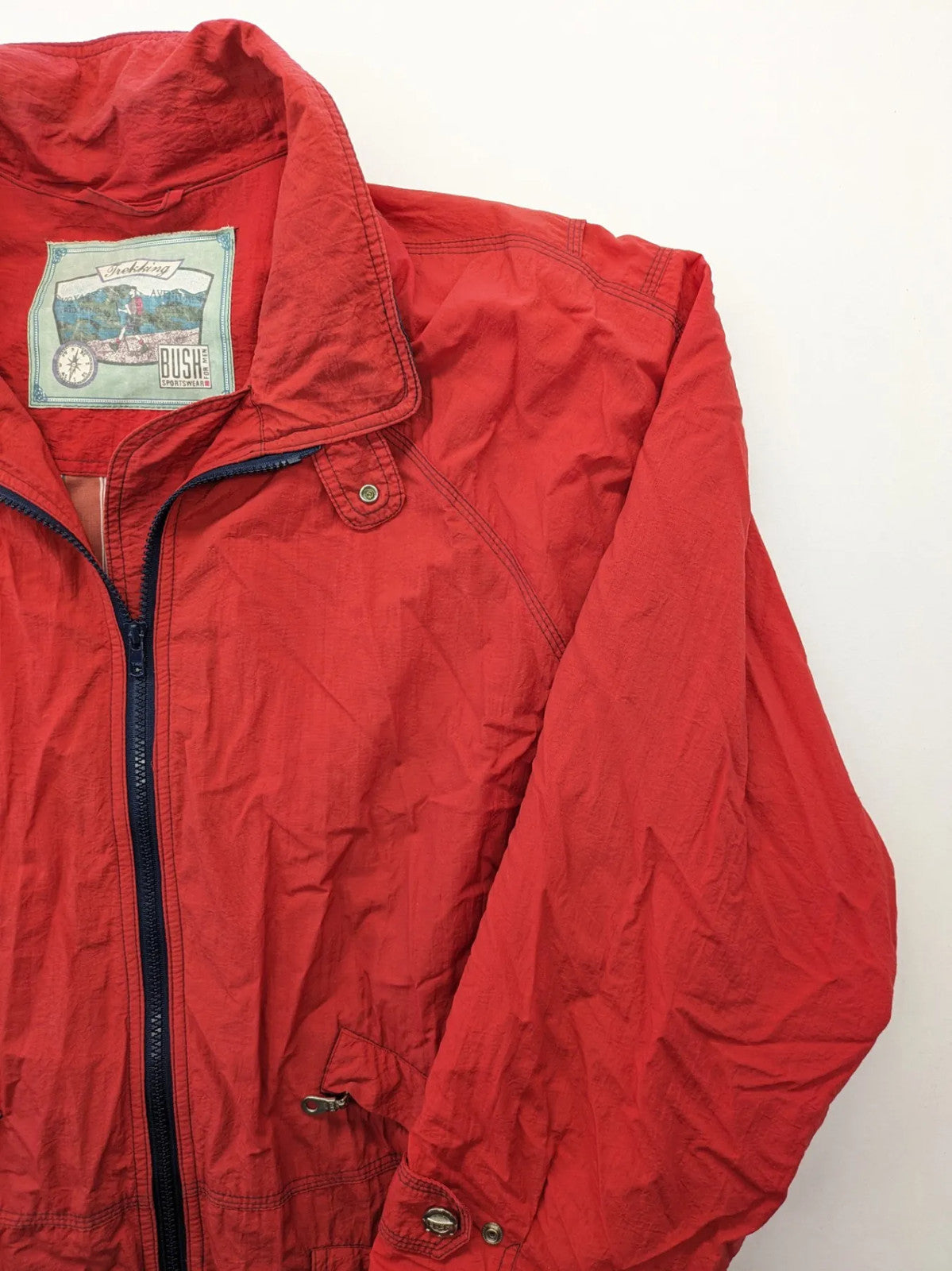 Bush Sportswear red trekking jacket with front zipper, multiple pockets, and striped lining.