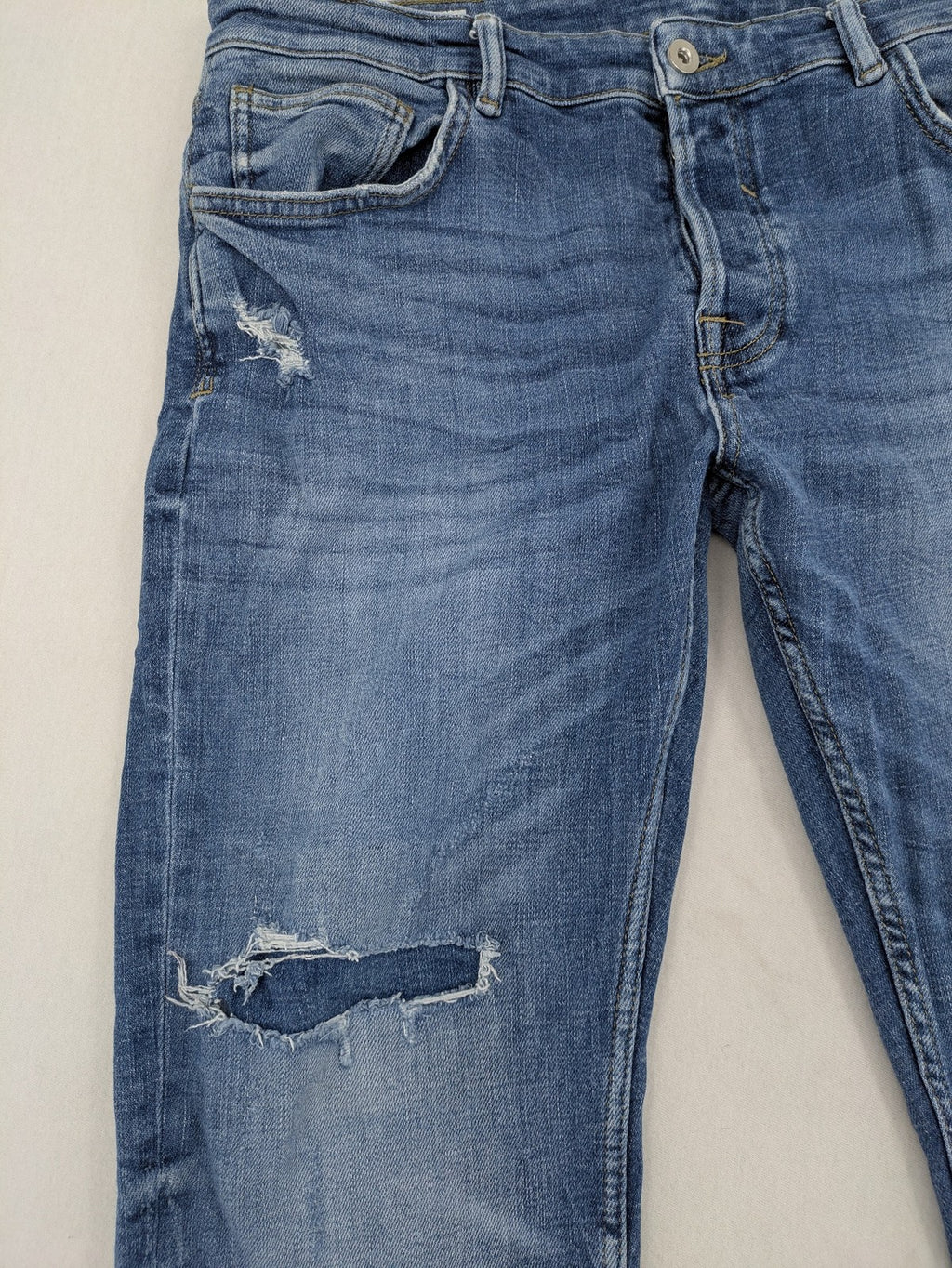 Zara blue straight jeans with distressed ripped knees and button-fly closure.