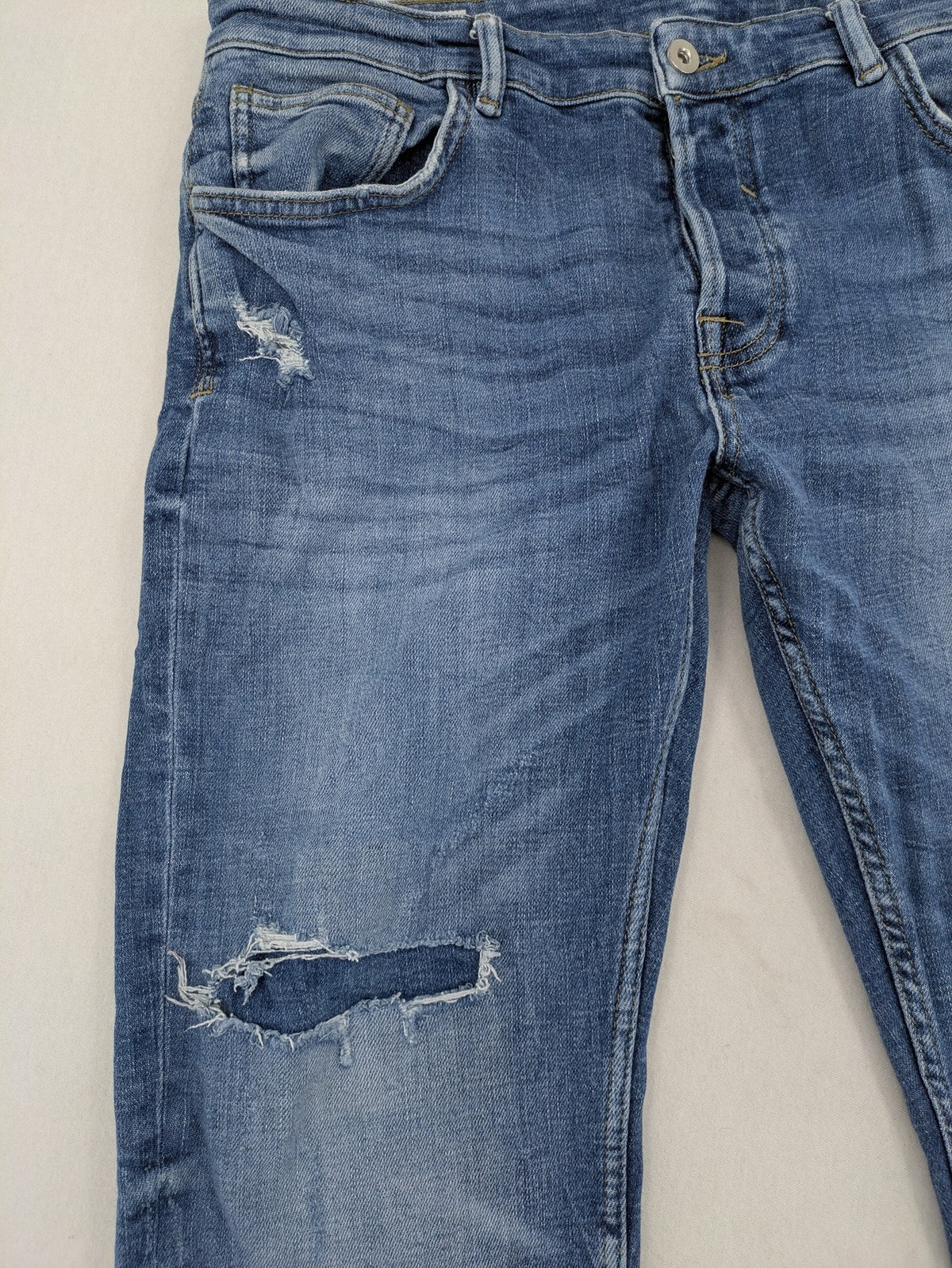 Zara blue straight jeans with distressed ripped knees and button-fly closure.