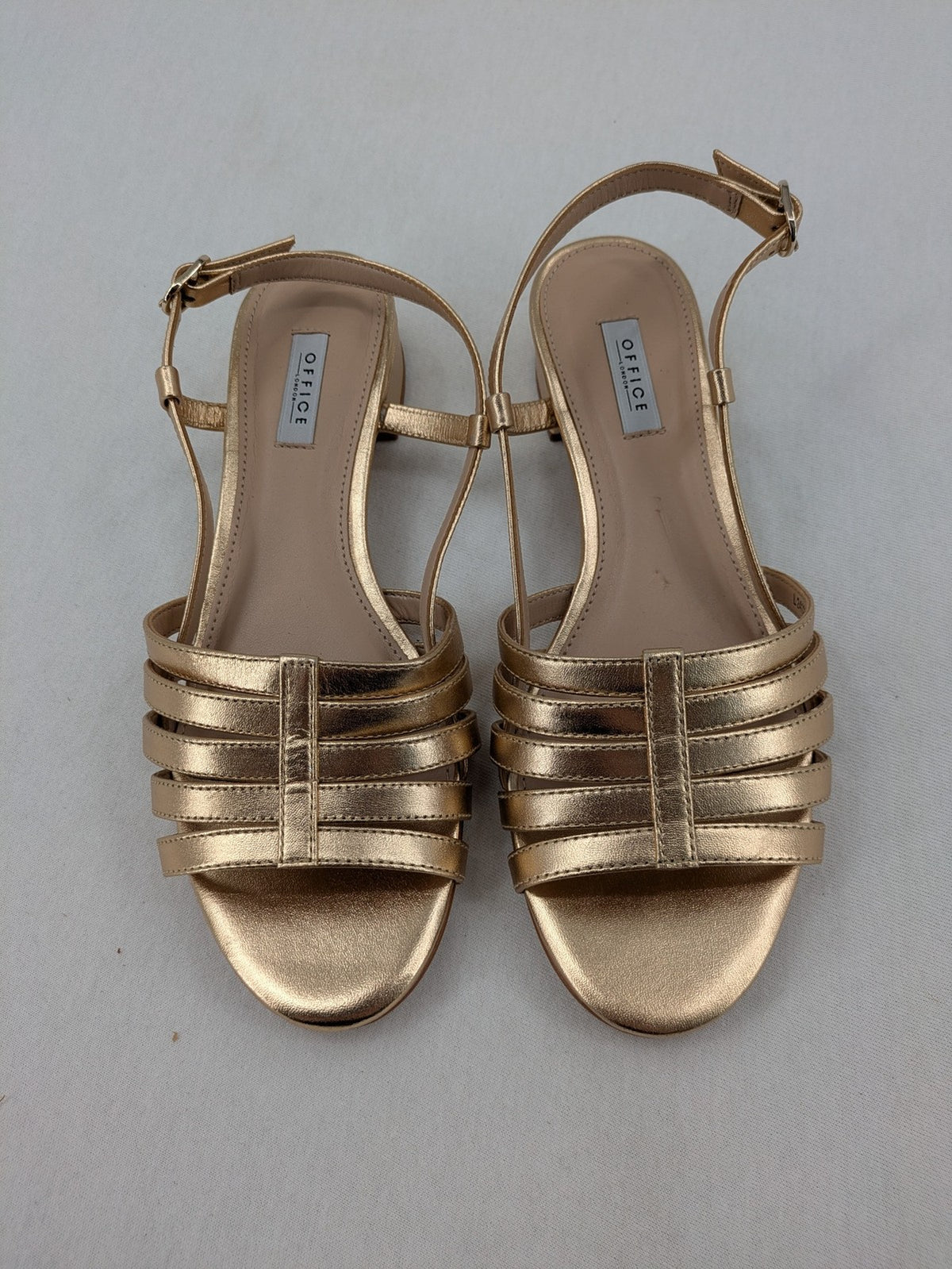 Office London gold metallic sandals with adjustable ankle strap and block heel design.