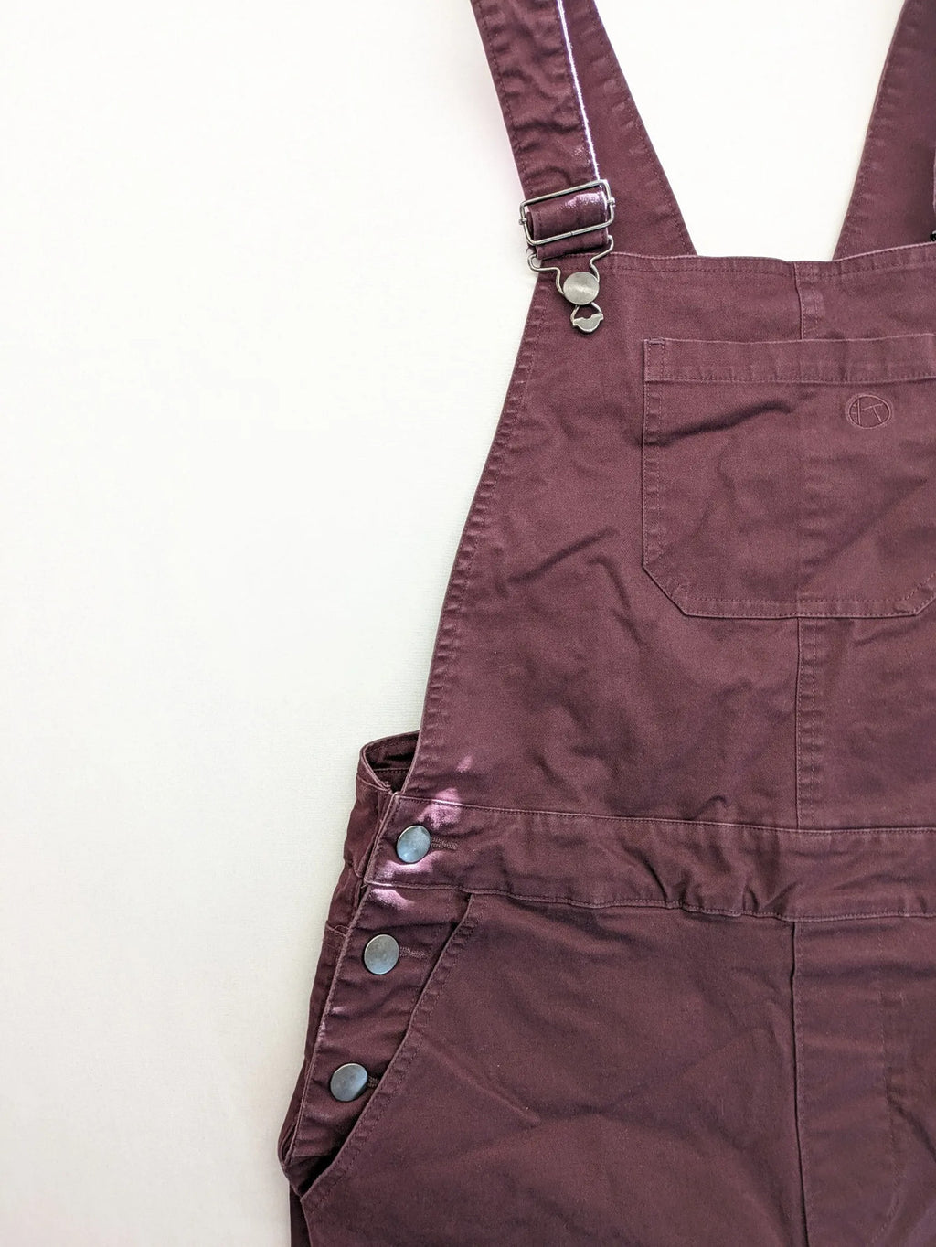 Kazane burgundy overalls with adjustable straps, side button placket, and chest pocket.