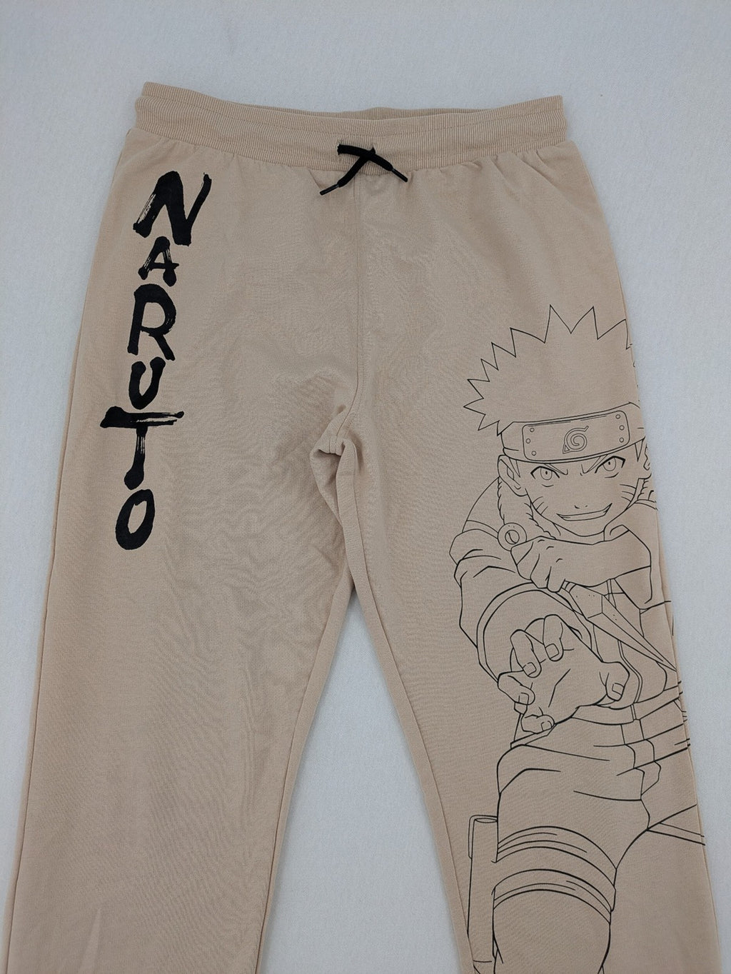 Naruto Shippuden beige joggers featuring Naruto Uzumaki graphic and logo print.