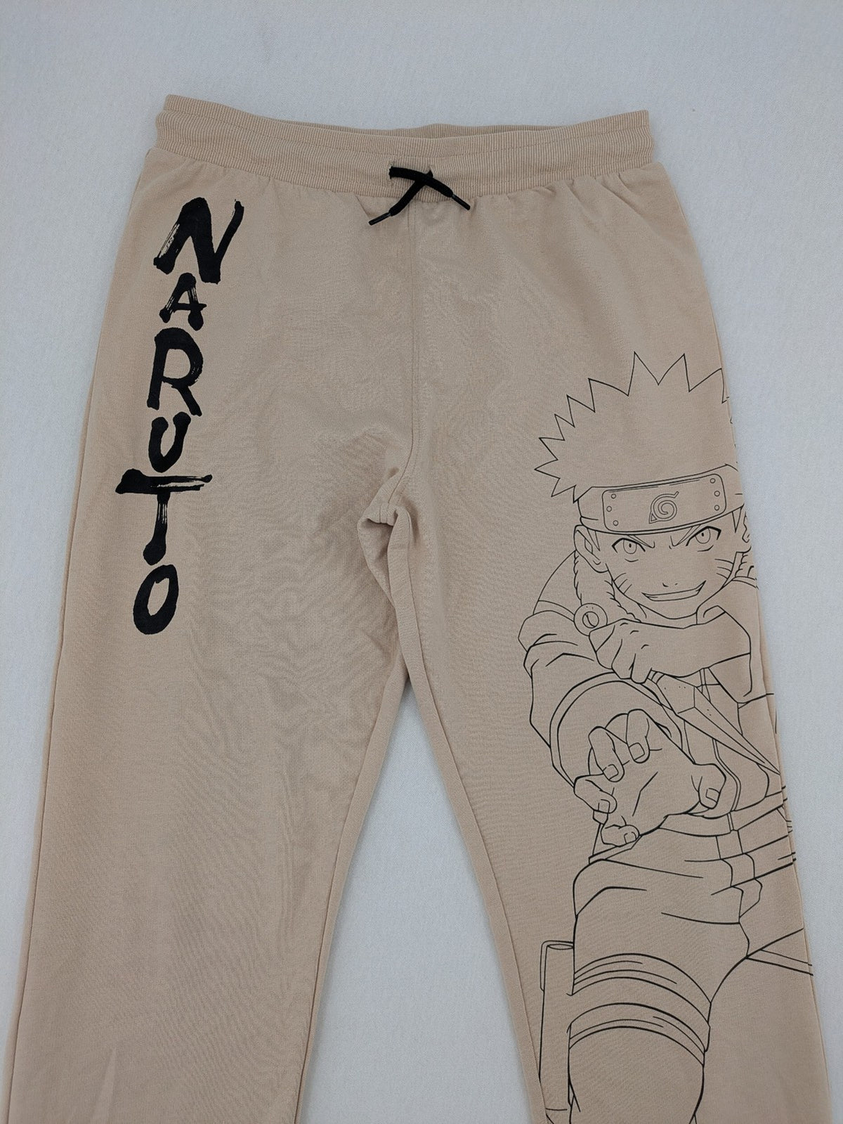 Naruto Shippuden beige joggers featuring Naruto Uzumaki graphic and logo print.