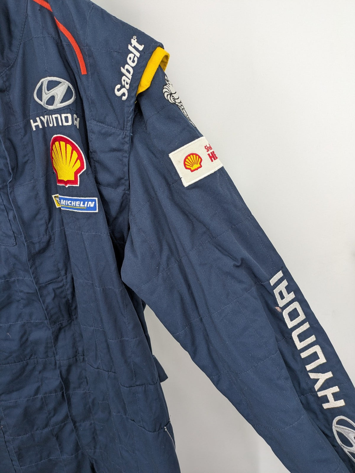 Hyundai Motorsport Sabelt racing suit navy blue with embroidered Shell and Michelin logos.