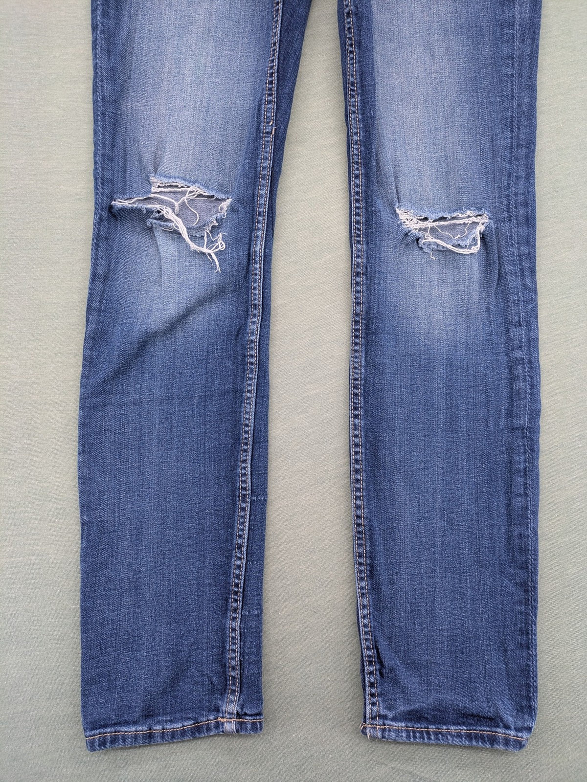 H&M blue skinny jeans with distressed knee details and classic 5-pocket design.