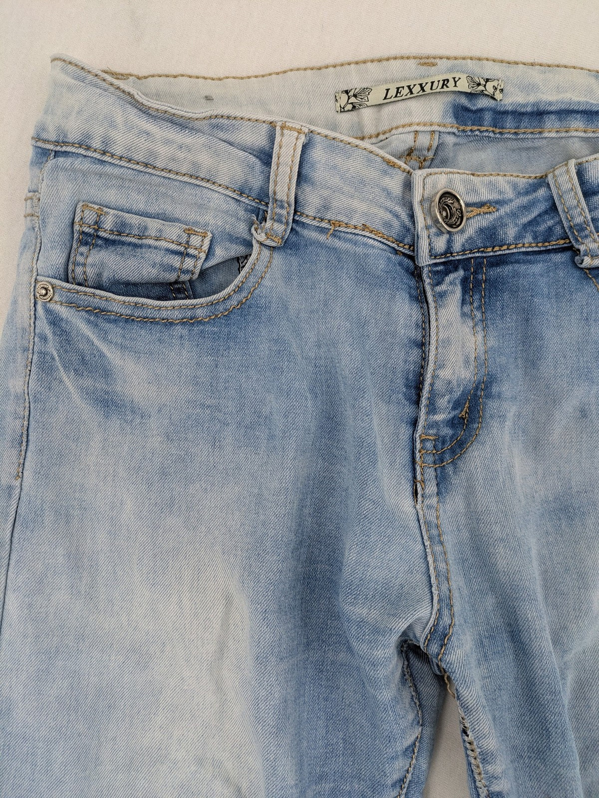 Lexxury blue skinny jeans distressed with knee rips and light wash finish.