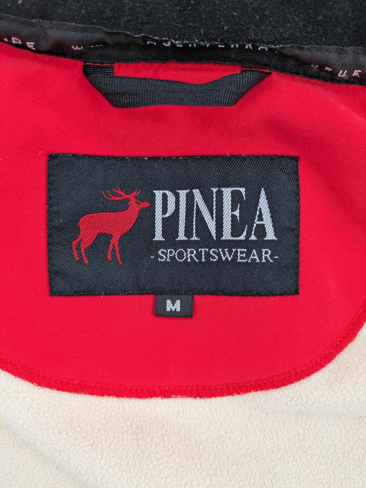 Pinea red softshell jacket with adjustable hood and fleece lining, multiple zippered pockets.