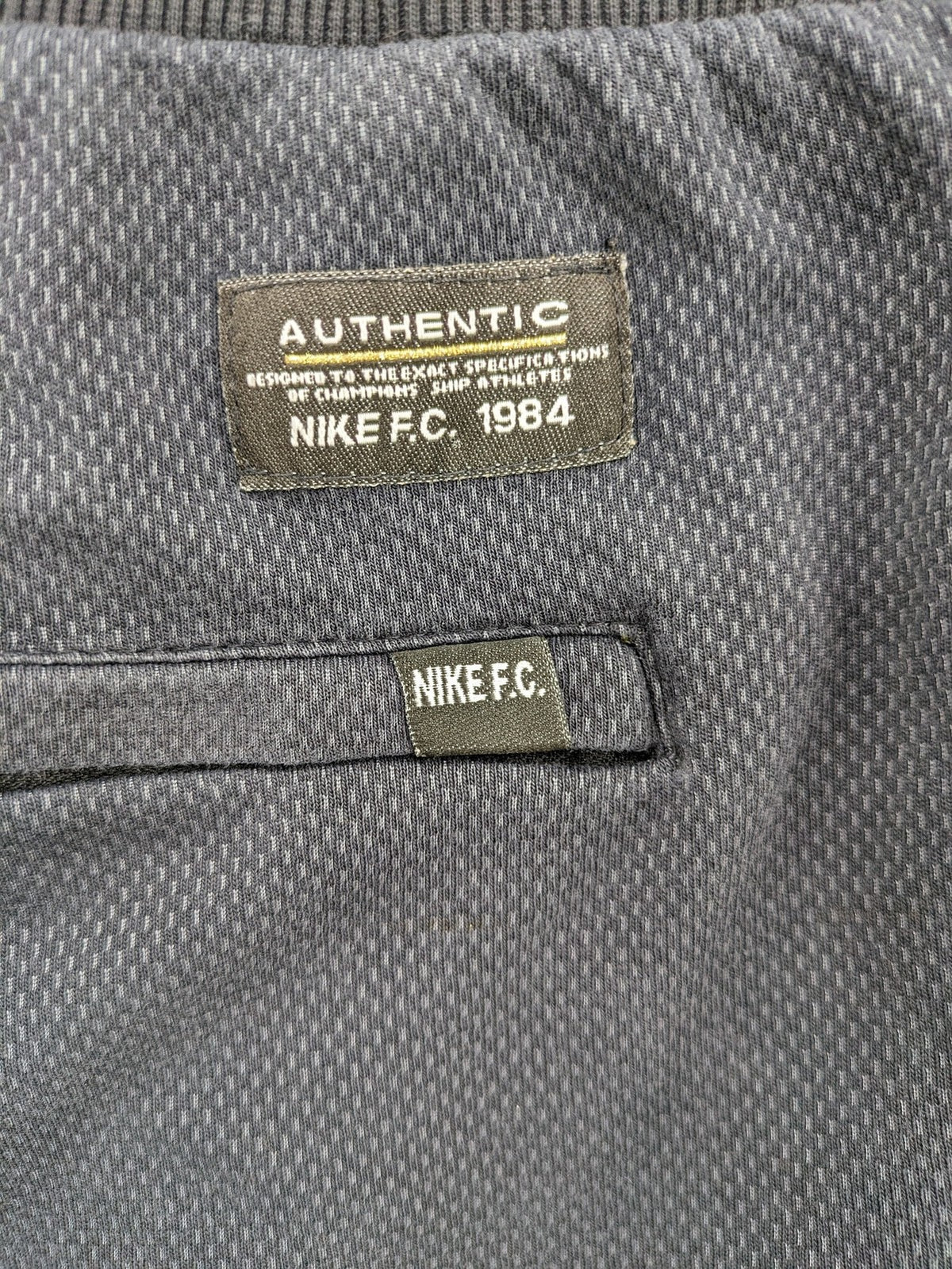 Nike F.C. grey jogger pants with elastic waistband, side pockets, and embroidered Swoosh logo.