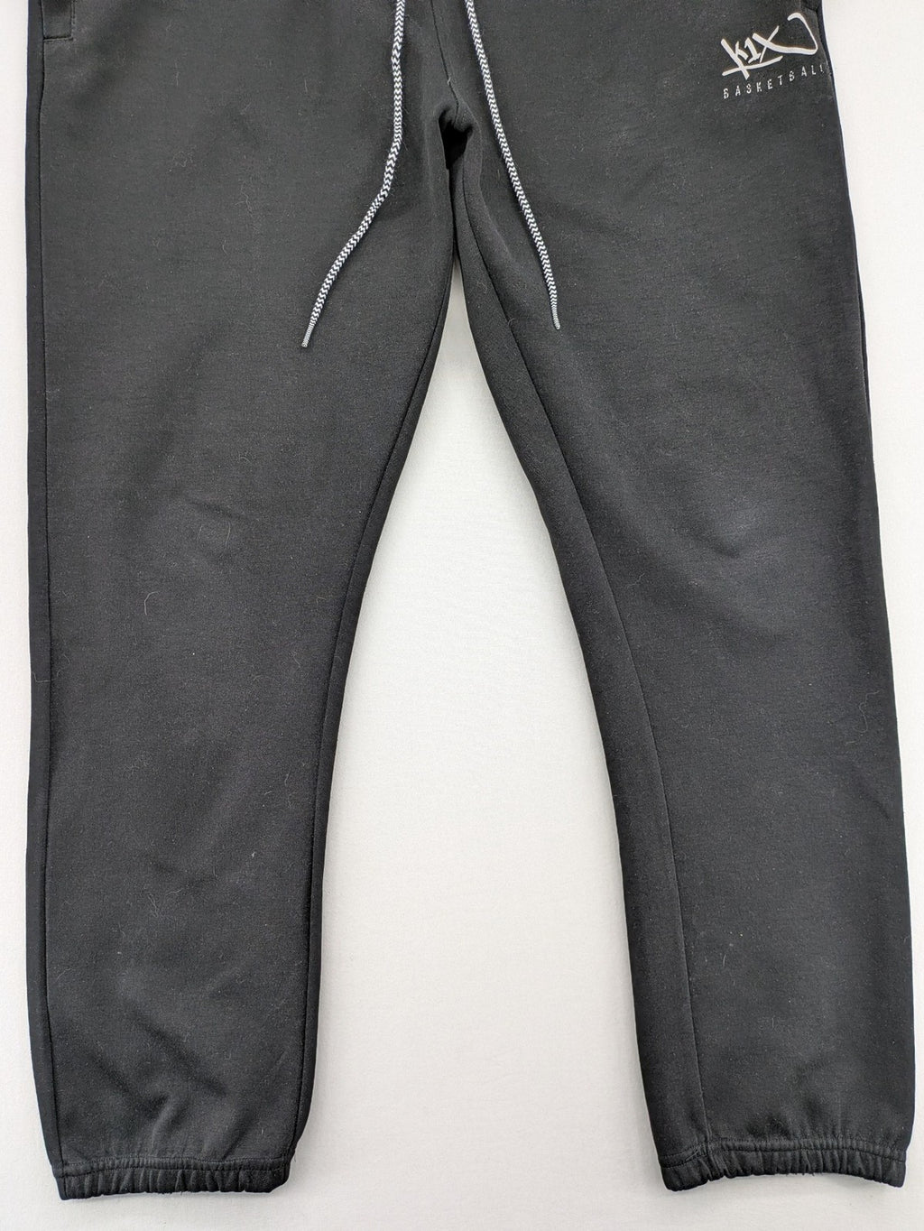 K1X grey joggers with white basketball logo, elastic waistband, and cuffed ankles.