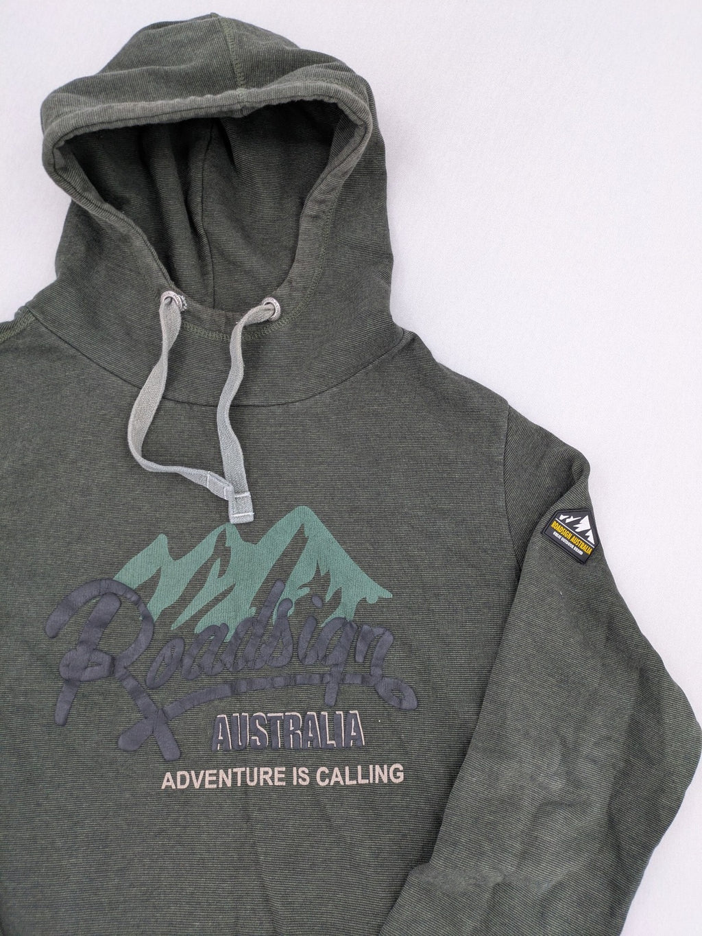 Roadsign Australia green hoodie with mountain graphic print and logo patch on sleeve.