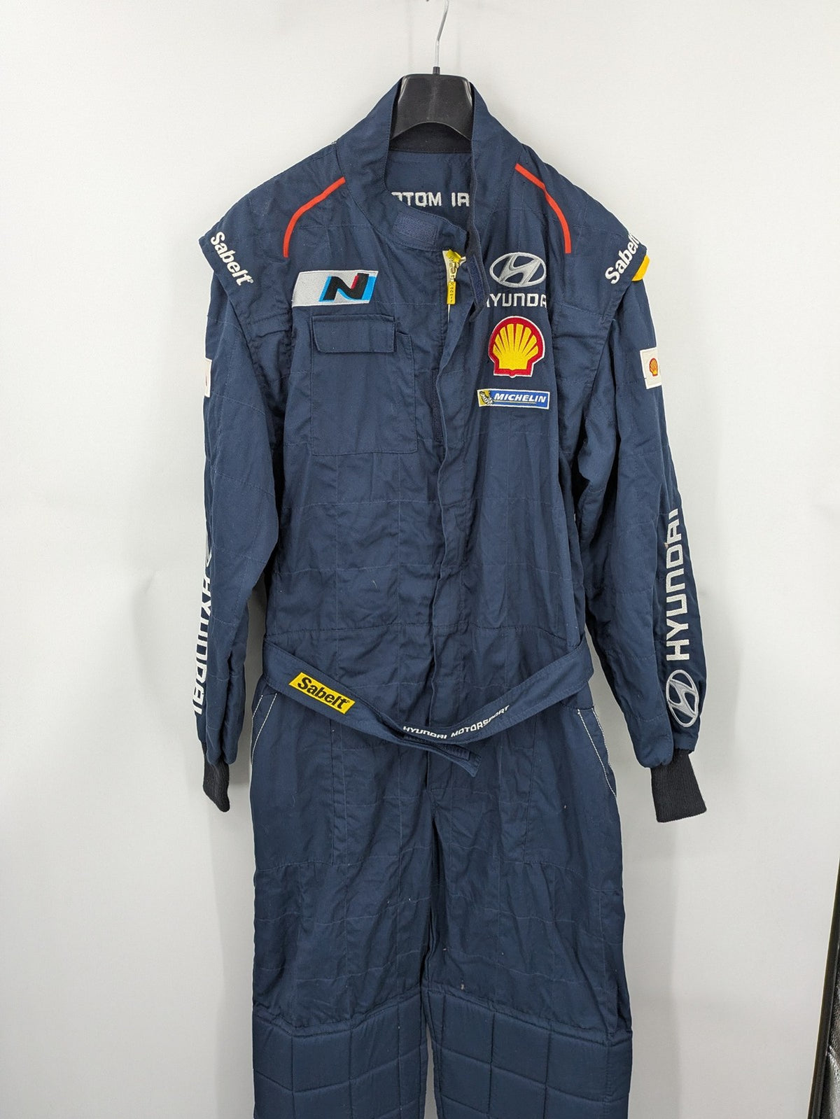 Hyundai Motorsport Sabelt racing suit navy blue with embroidered Shell and Michelin logos.