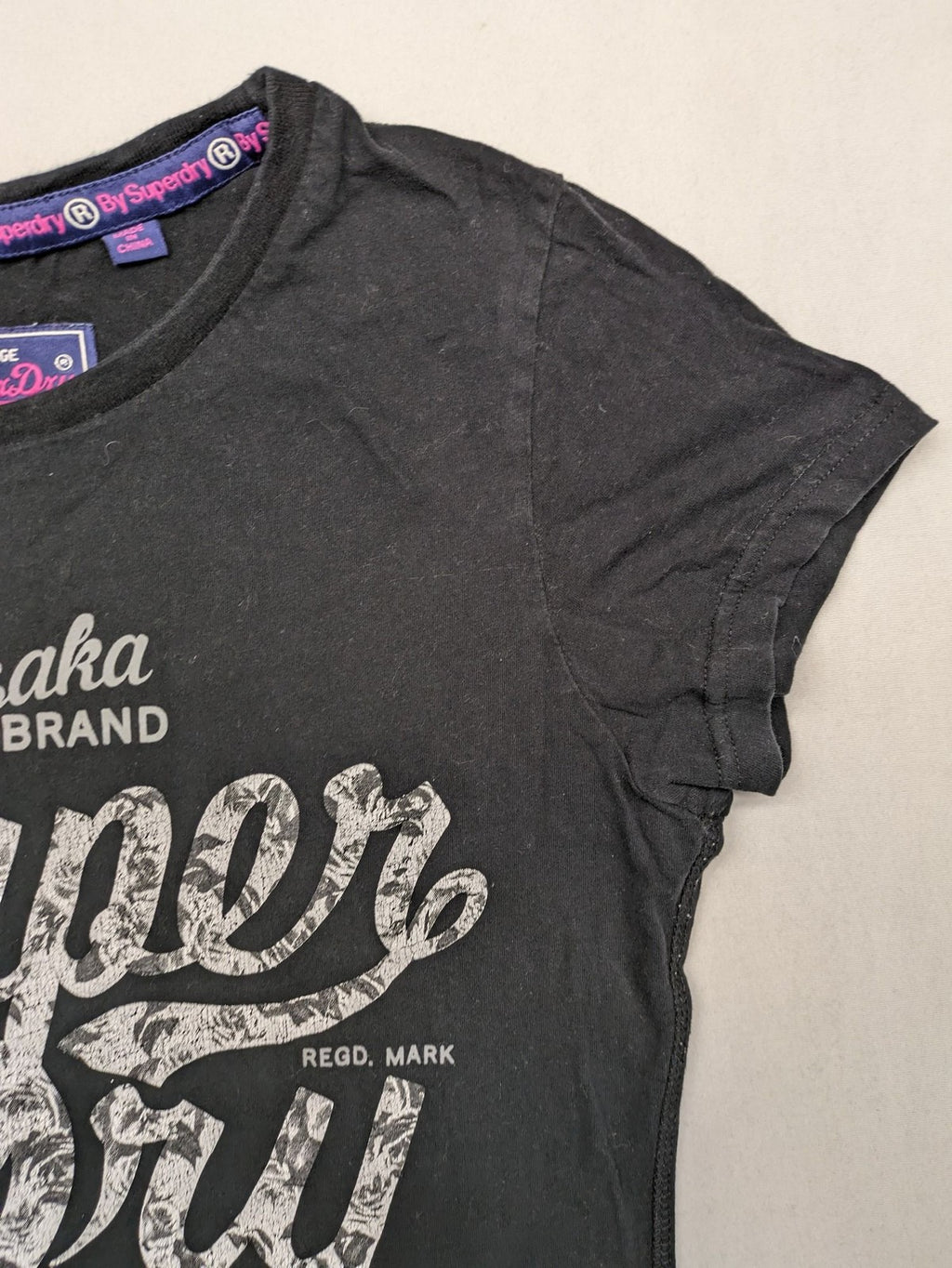 Superdry black t-shirt with large Osaka Brand logo and subtle floral pattern.