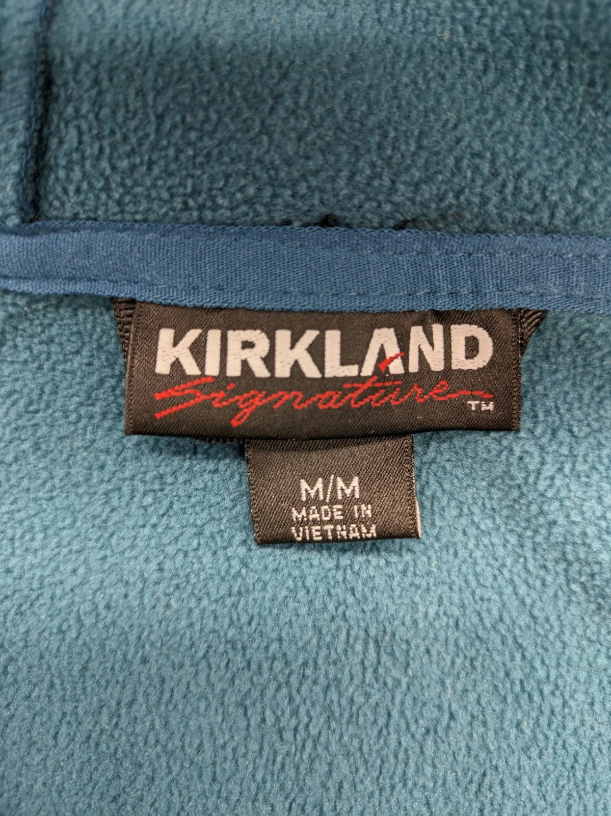Kirkland Signature blue softshell jacket with hood, fleece lining, and zippered pockets.