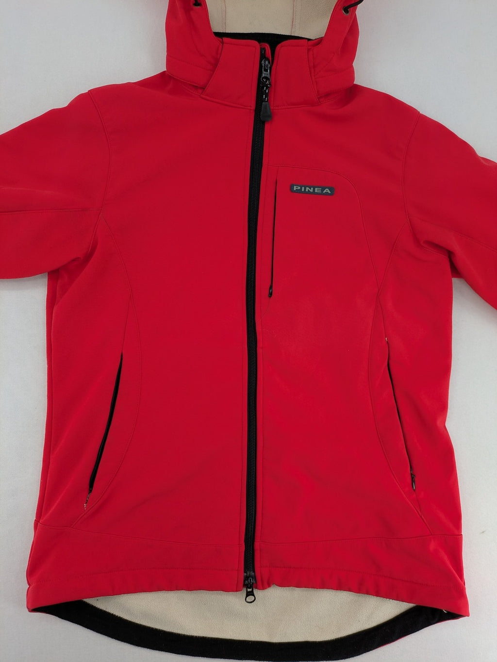 Pinea red softshell jacket with adjustable hood and fleece lining, multiple zippered pockets.