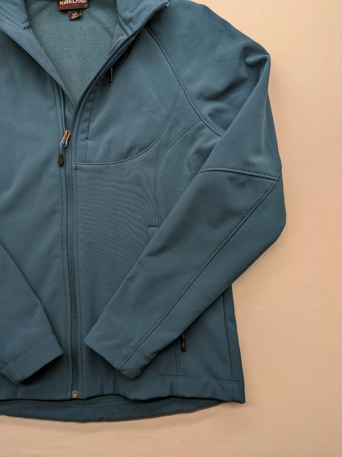Kirkland Signature blue softshell jacket with hood, fleece lining, and zippered pockets.