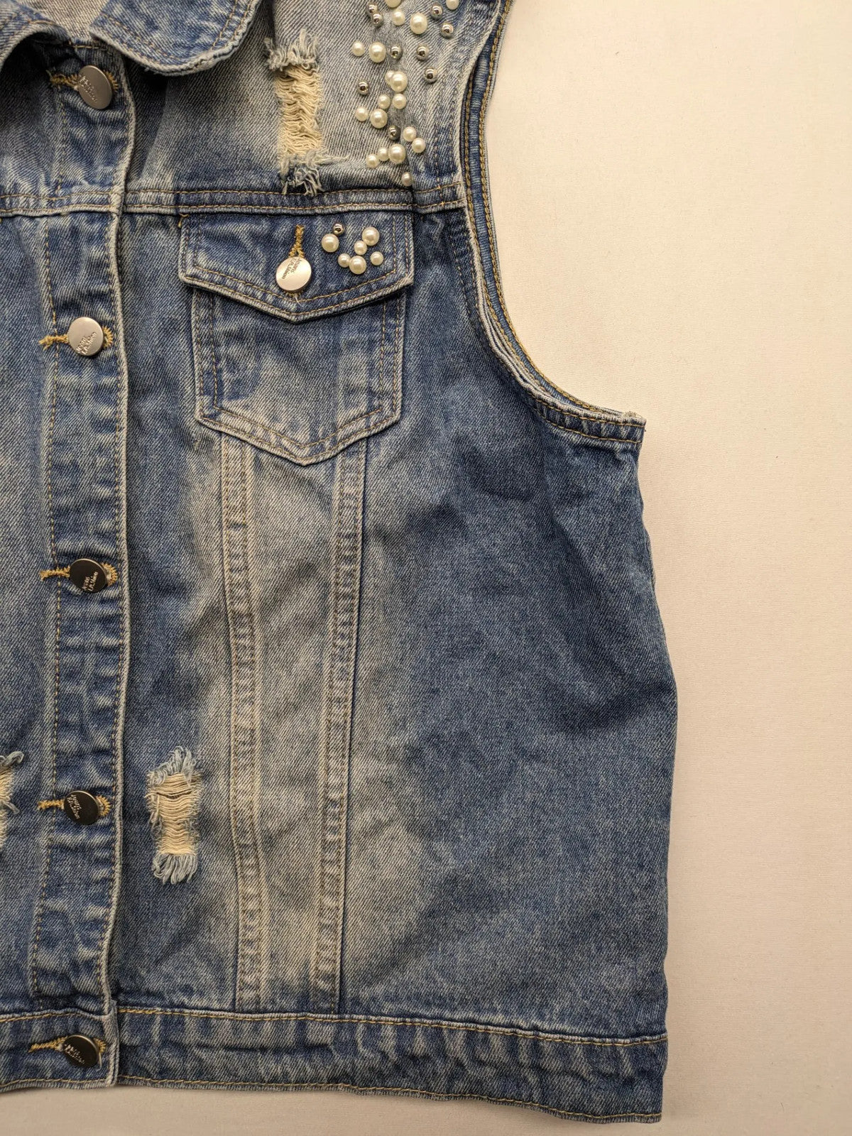Damen Jeansjacke blau ärmellos mit Perlenverzierung, distressed Details und Knopfleiste.