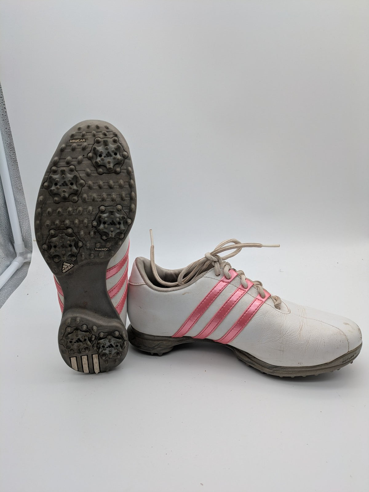 Adidas white golf shoes with pink stripes, Thintech and TRAXION technology, stylish design.