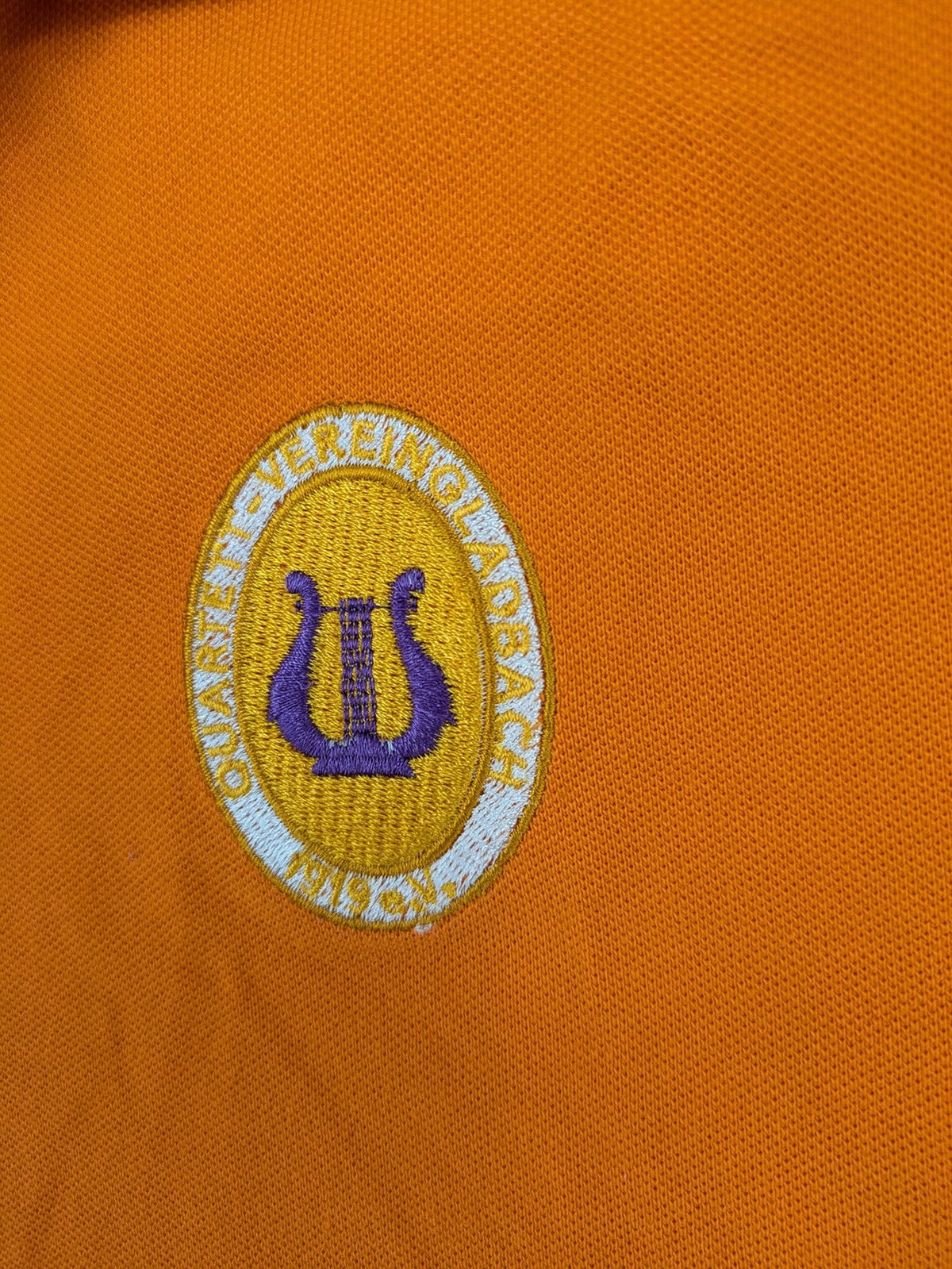 Teejays orange polo shirt with embroidered logo, classic collar, and button placket.