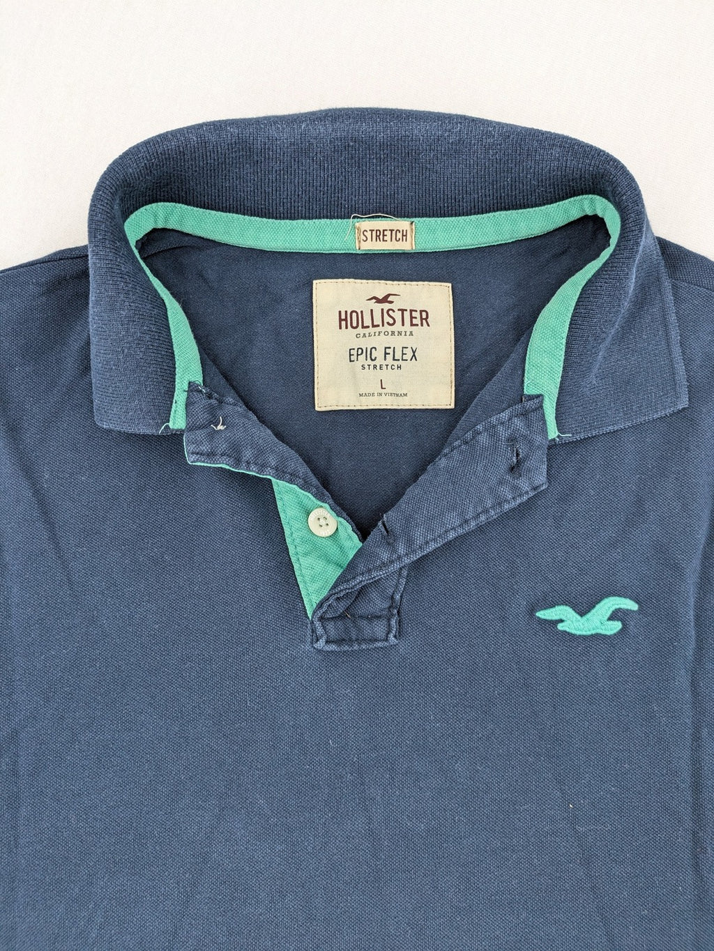 Hollister polo shirt navy blue with embroidered seagull logo and green trim.