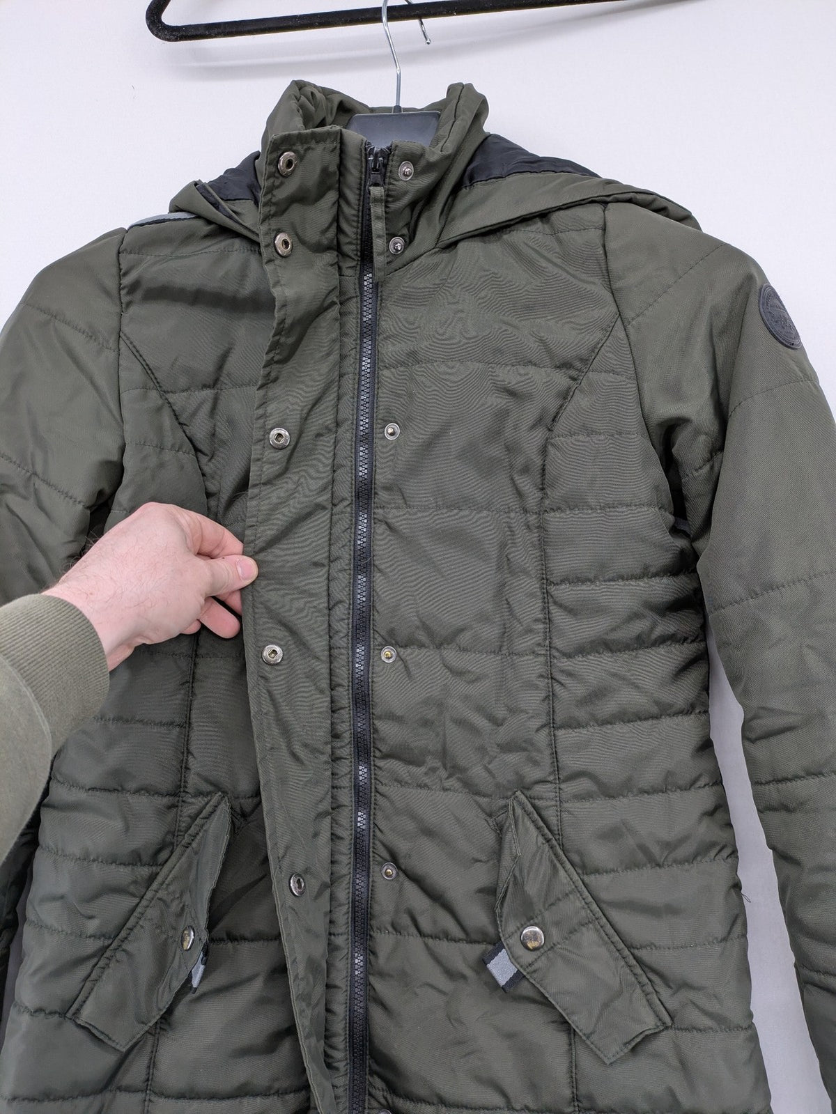 Vero Moda green puffer coat with quilted design and hood, featuring zipper and button closure.