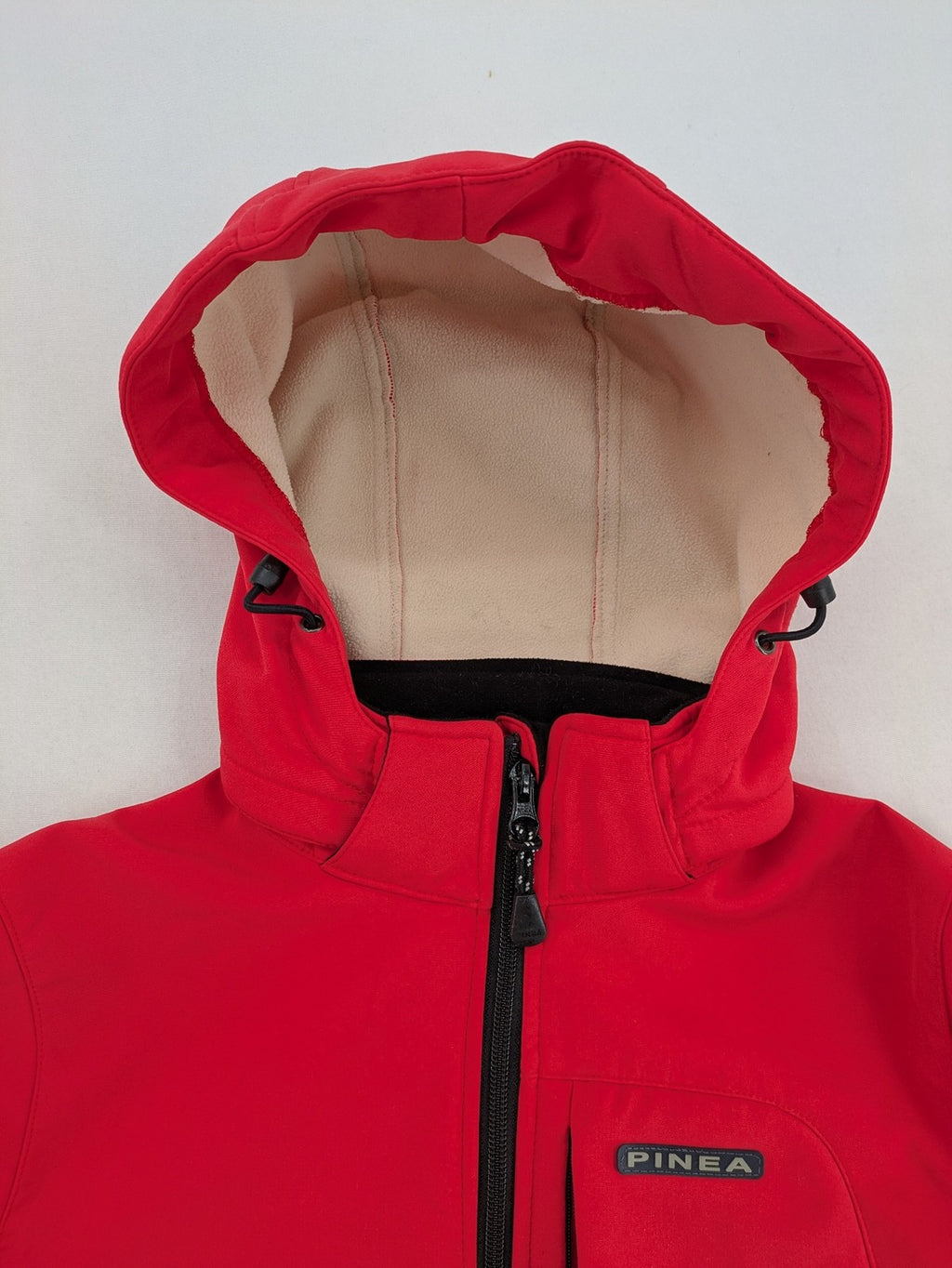 Pinea red softshell jacket with adjustable hood and fleece lining, multiple zippered pockets.