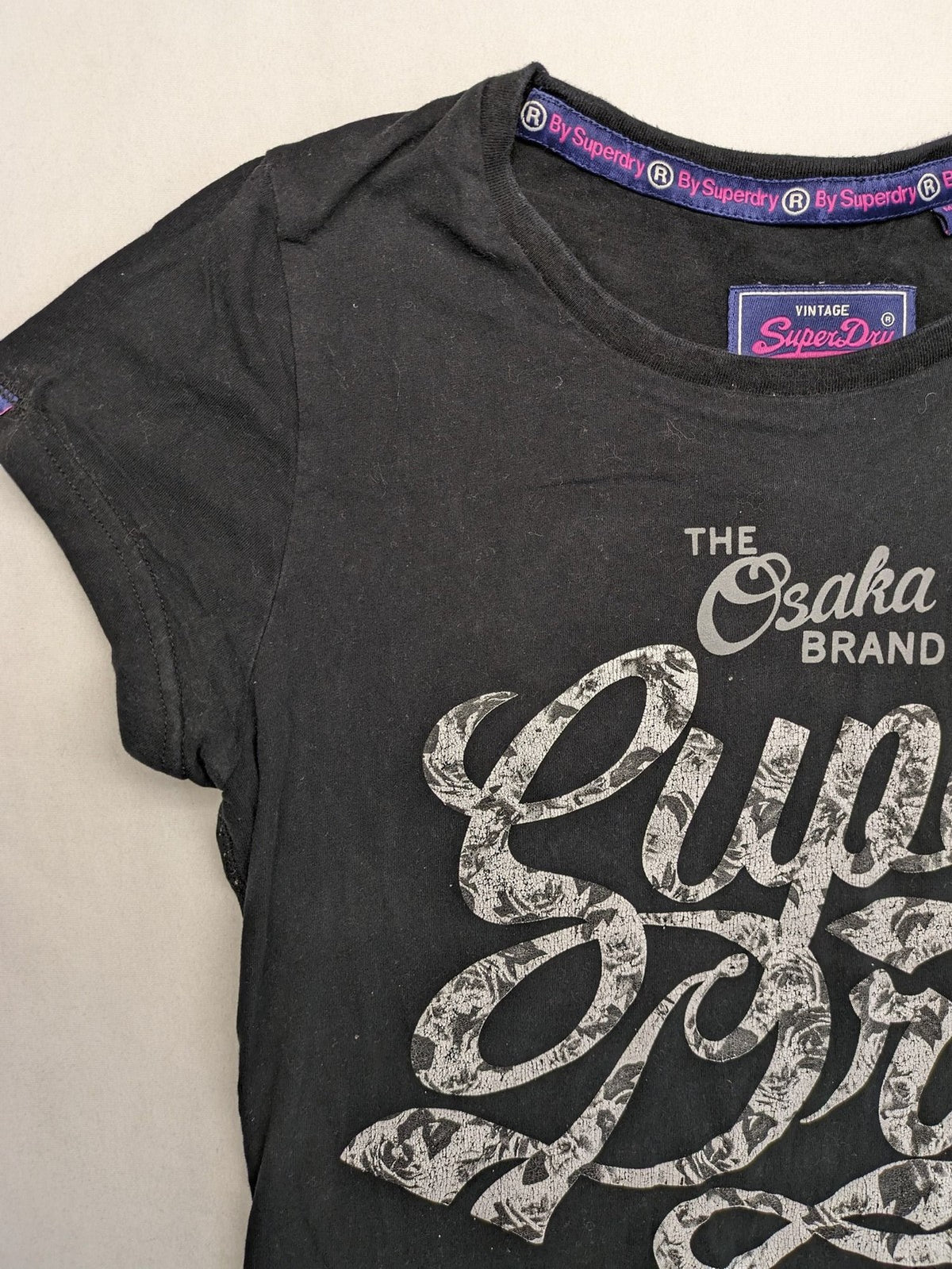 Superdry black t-shirt with large Osaka Brand logo and subtle floral pattern.