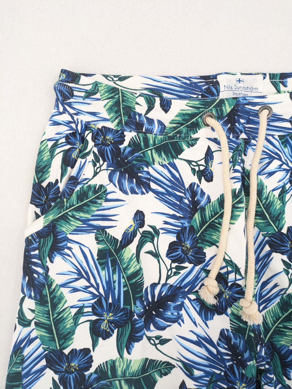 Nils Sundström blue and green tropical floral shorts with white background and elastic waistband.