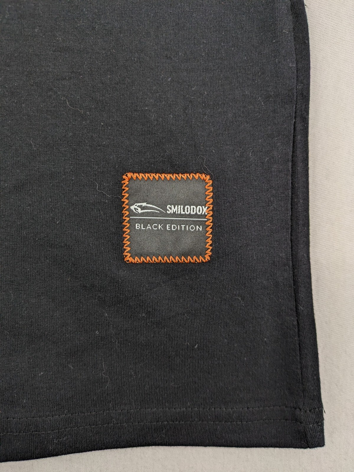 Smilodox black T-shirt minimalist design with subtle brand patch, 100% cotton.