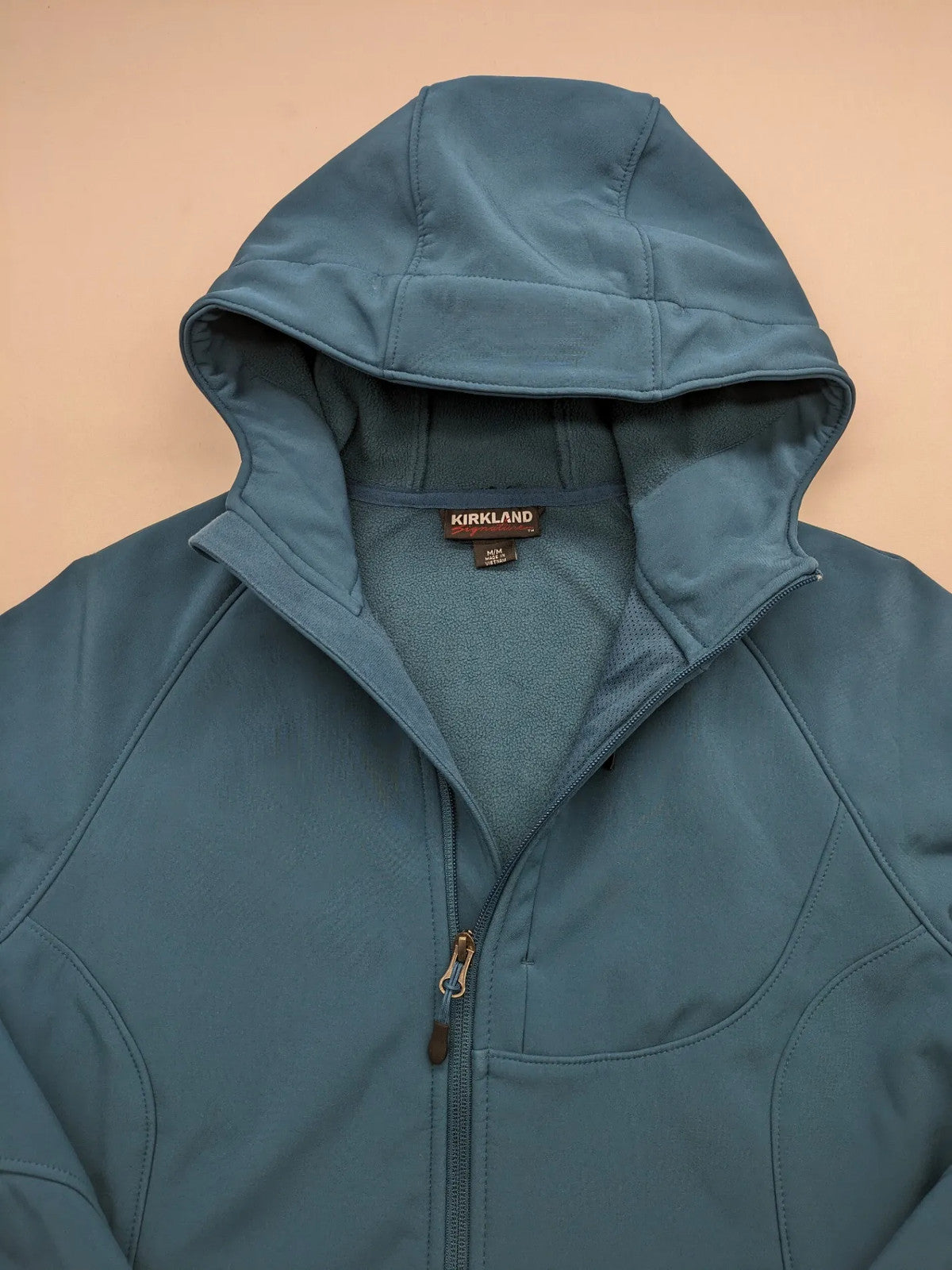 Kirkland Signature blue softshell jacket with hood, fleece lining, and zippered pockets.