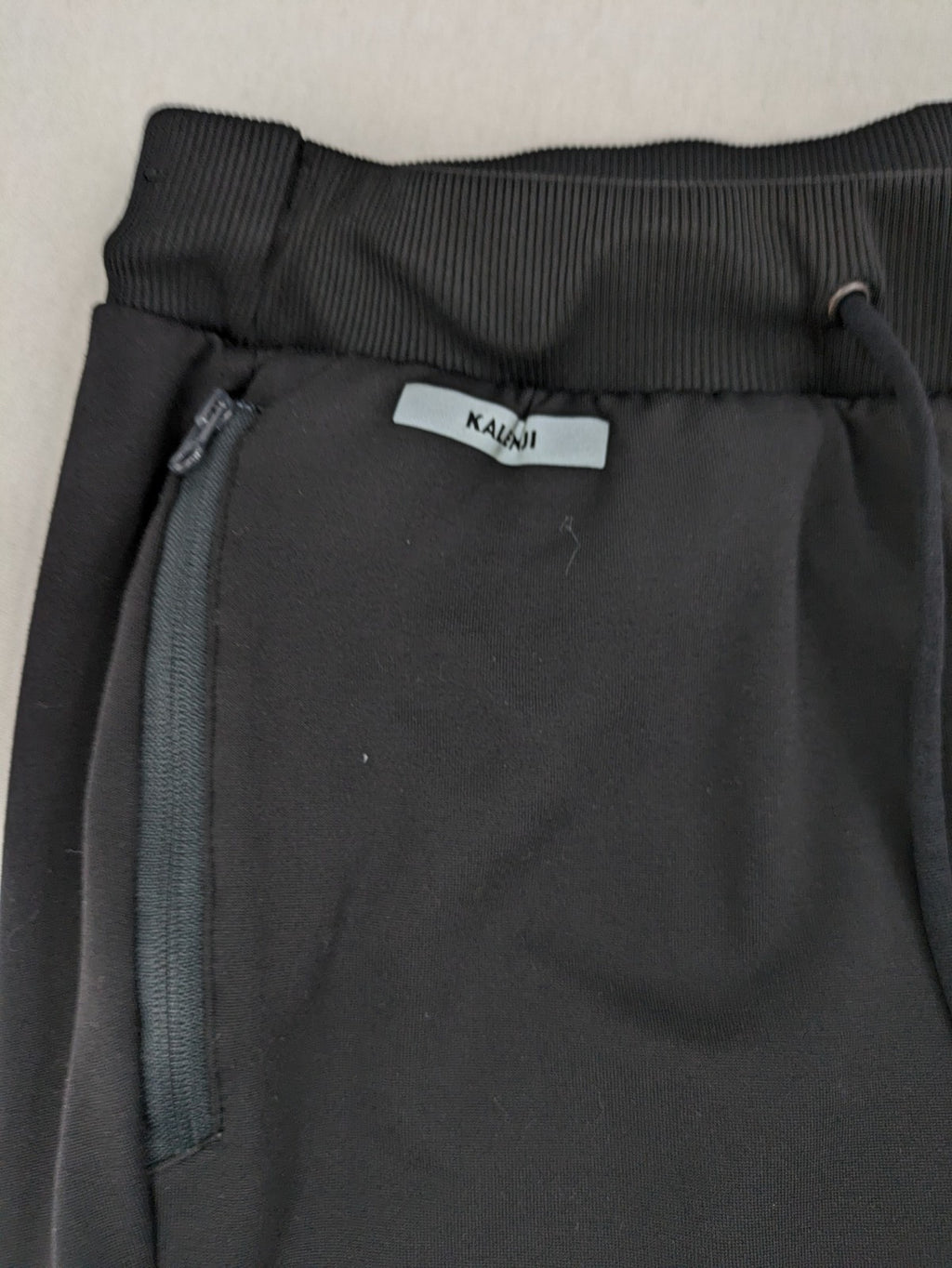 Kalenji black loungewear pants with grey accents and zippered side pockets.