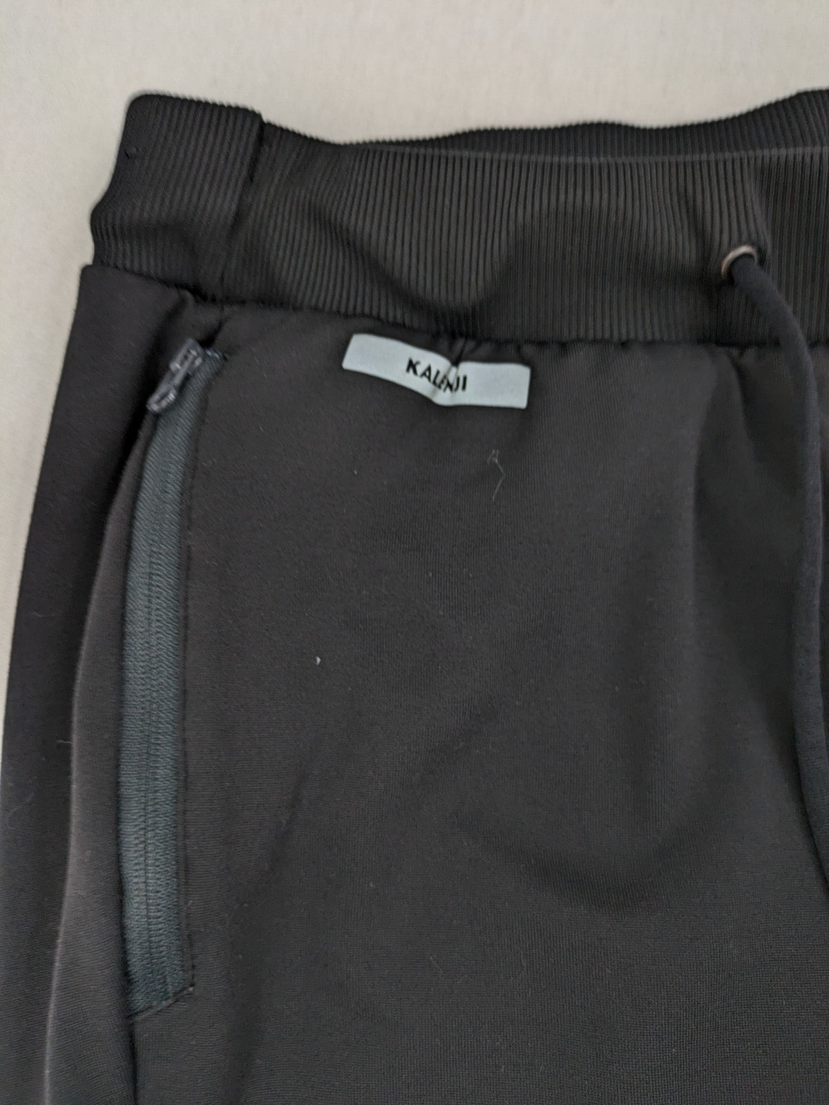 Kalenji black loungewear pants with grey accents and zippered side pockets.