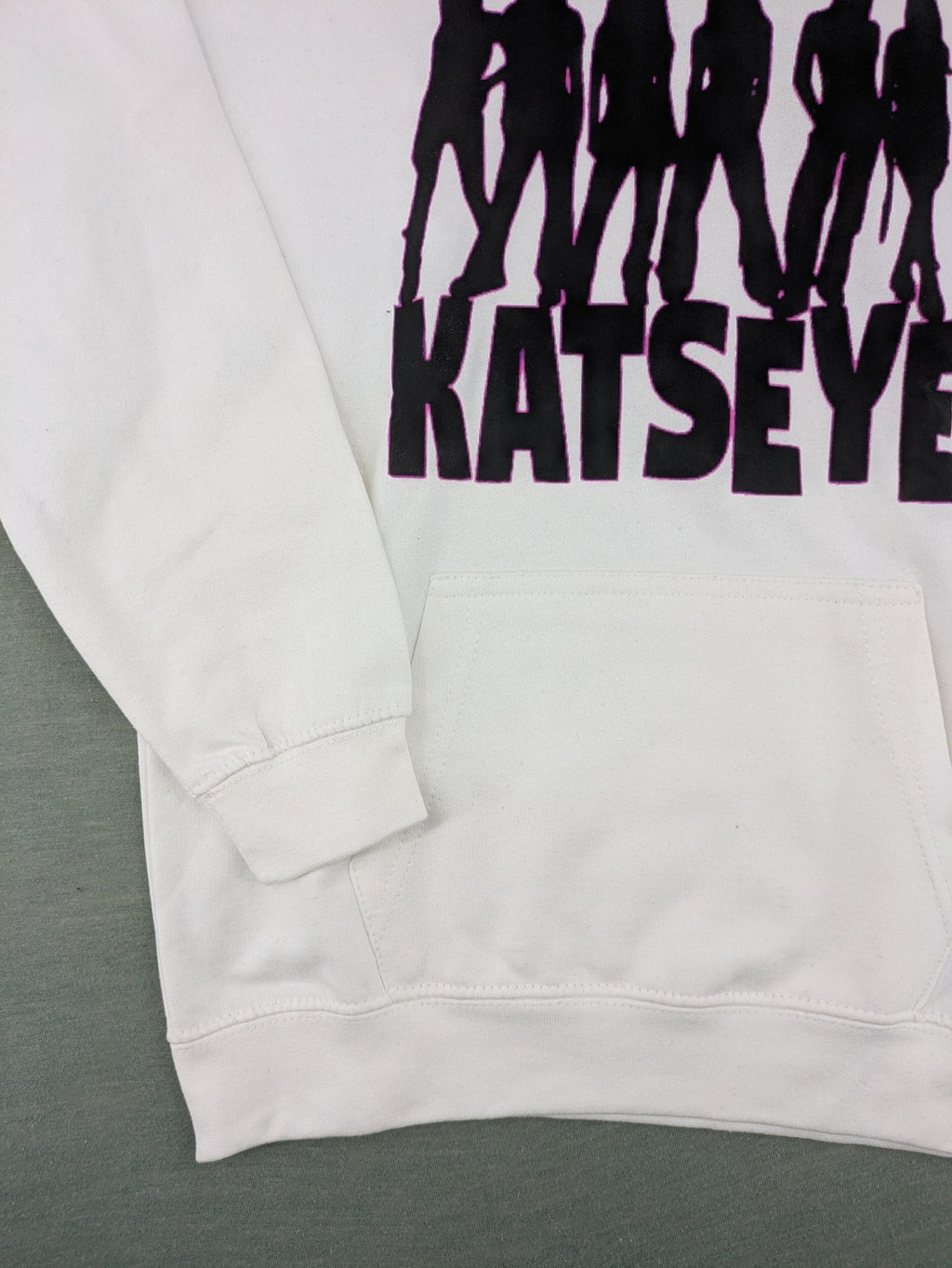 KATSEYE white zip-through hoodie with black silhouette graphic and logo, classic pullover style.