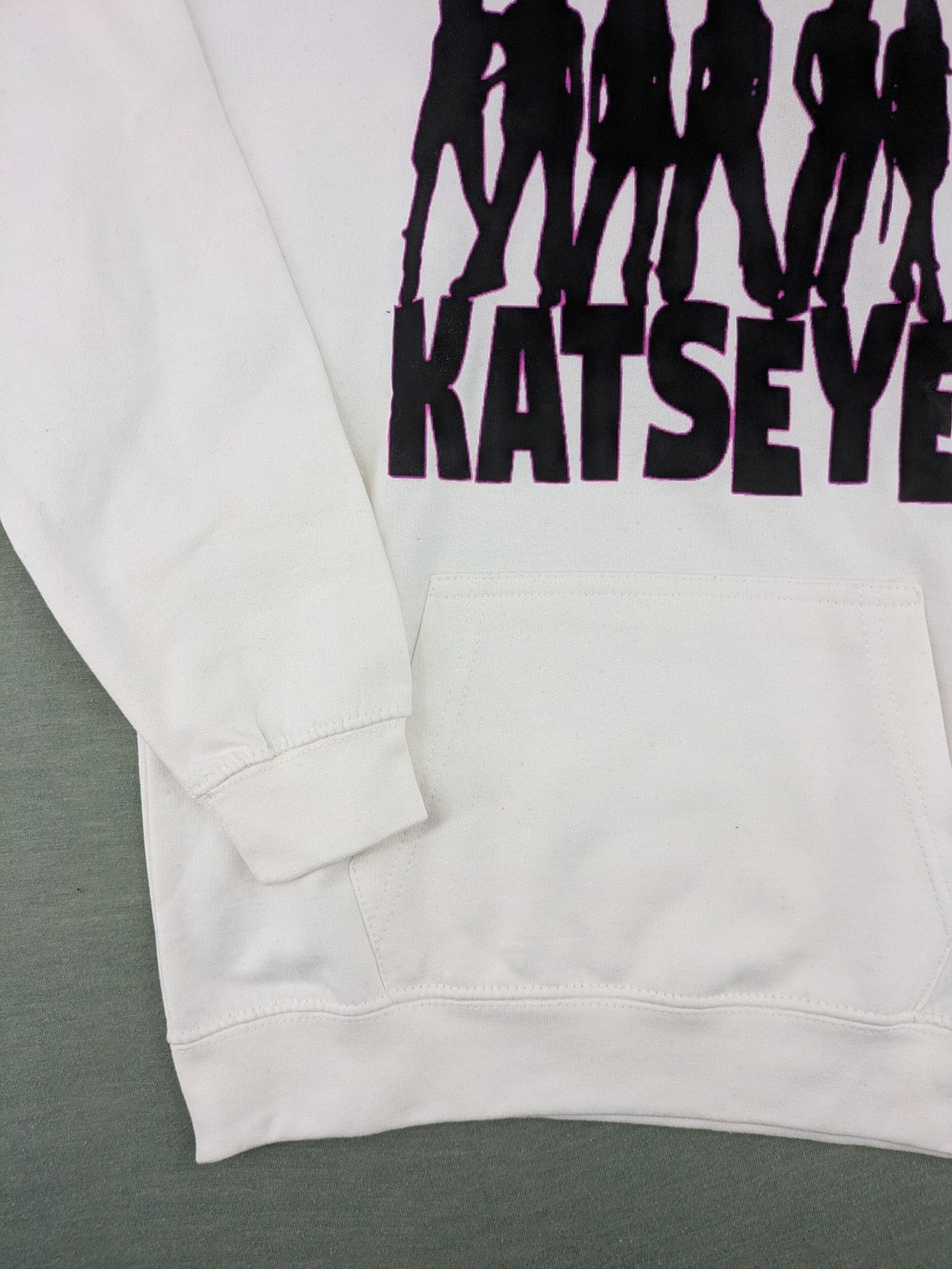 KATSEYE white zip-through hoodie with black silhouette graphic and logo, classic pullover style.