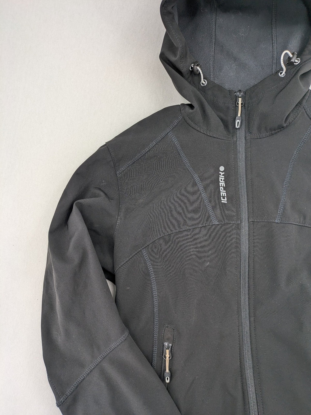 Icepeak black softshell jacket with fleece lining, adjustable hood, and zippered pockets.