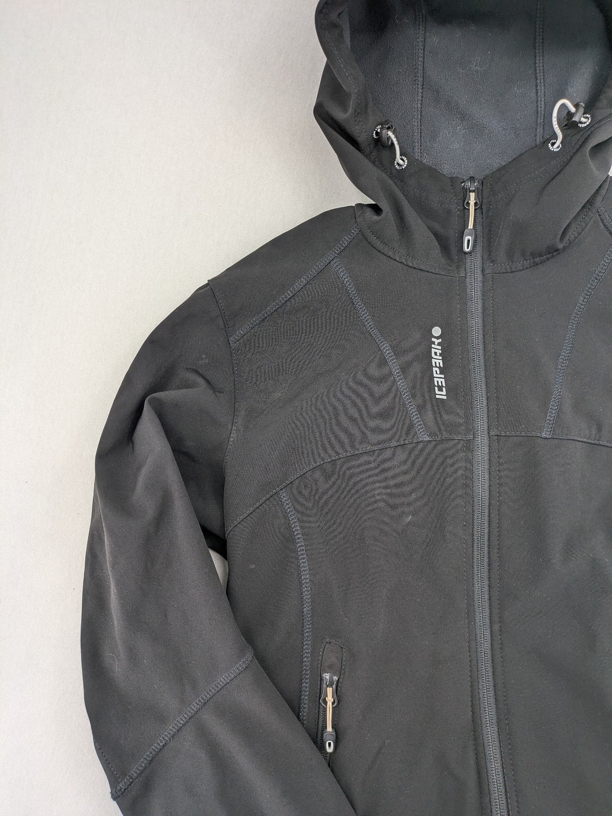 Icepeak black softshell jacket with fleece lining, adjustable hood, and zippered pockets.