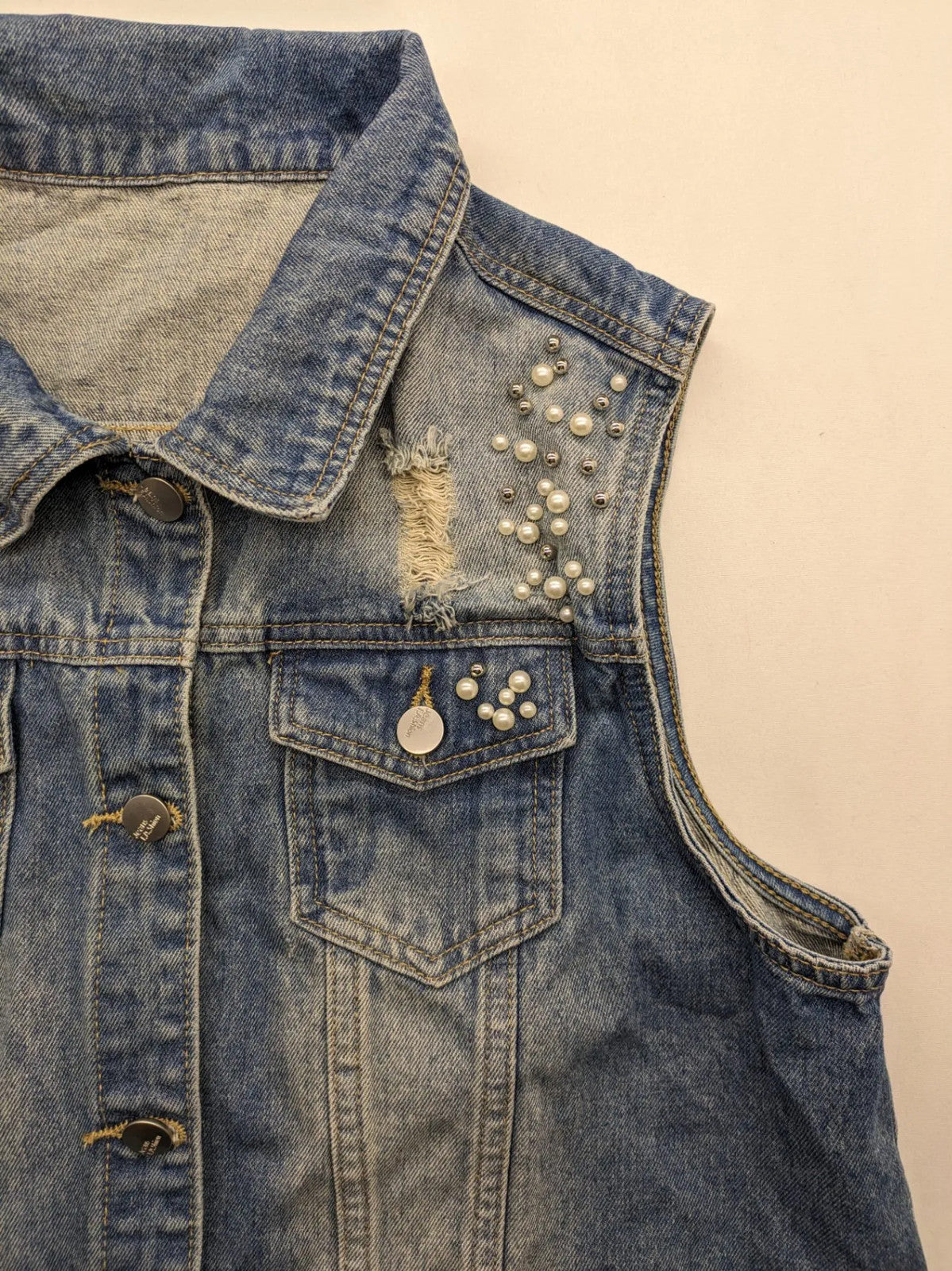 Damen Jeansjacke blau ärmellos mit Perlenverzierung, distressed Details und Knopfleiste.