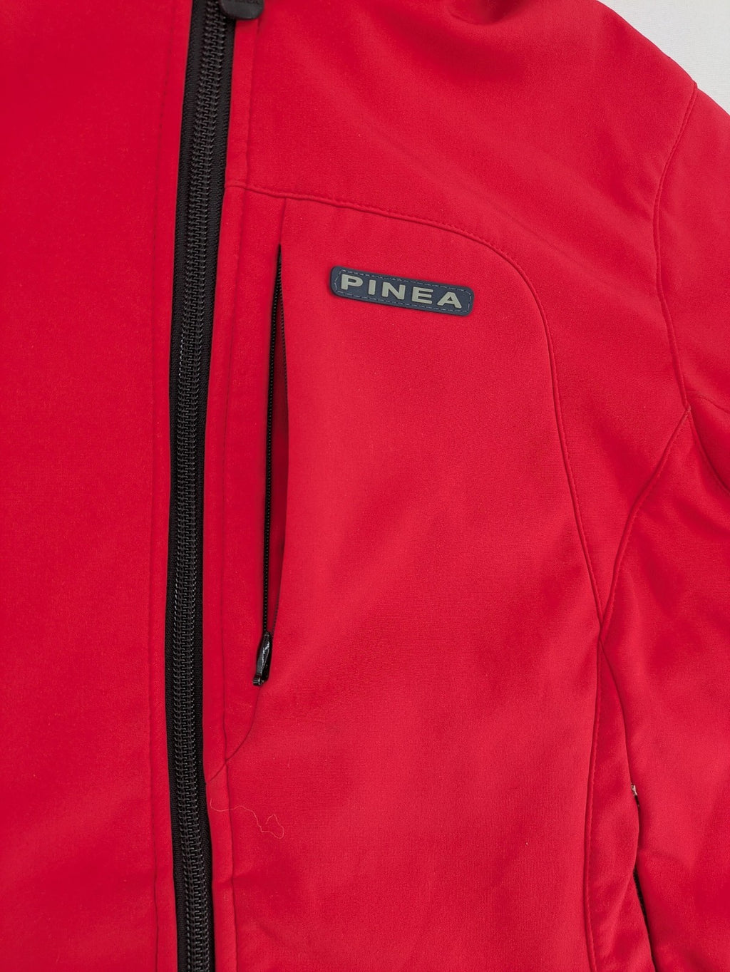 Pinea red softshell jacket with adjustable hood and fleece lining, multiple zippered pockets.