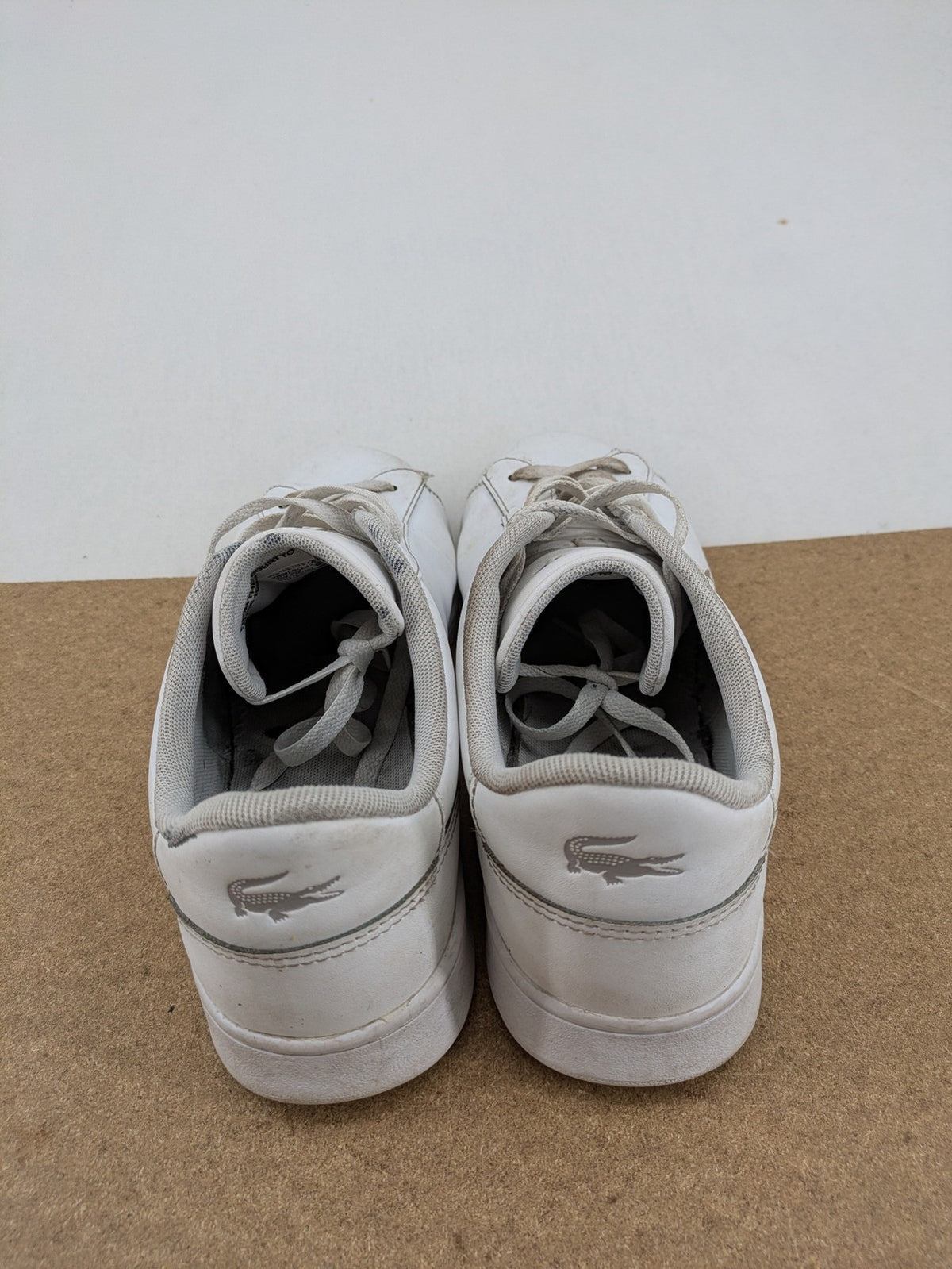 Lacoste cream low top sneakers with iconic crocodile logo and classic design.