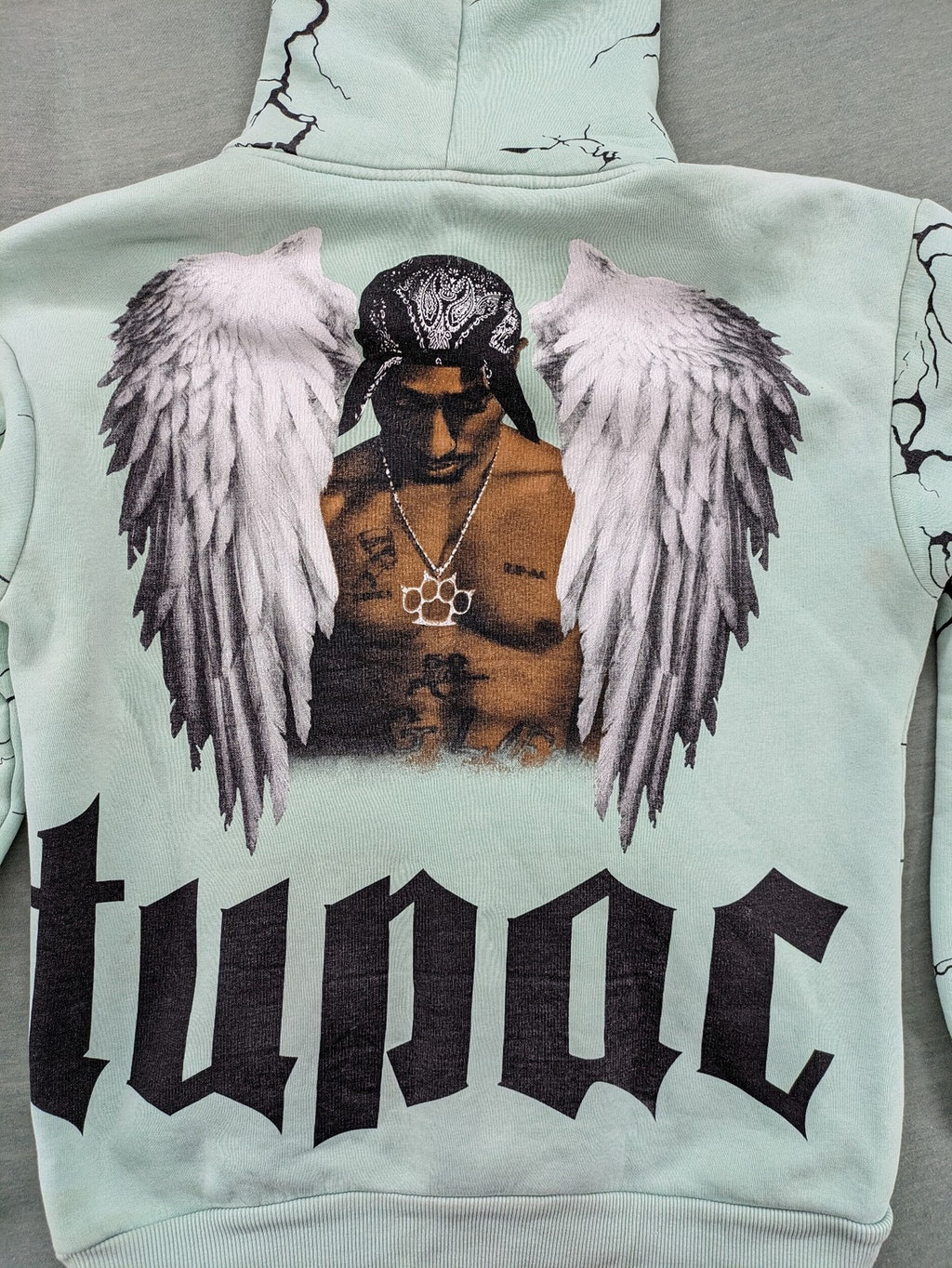 Tupac black and green zip-through hoodie with "Only God Can Judge Me" front print and angel wings graphic.