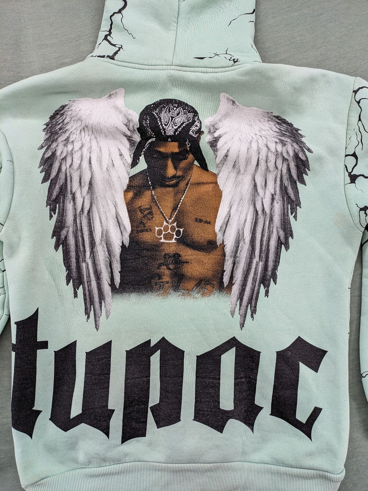 Tupac black and green zip-through hoodie with "Only God Can Judge Me" front print and angel wings graphic.