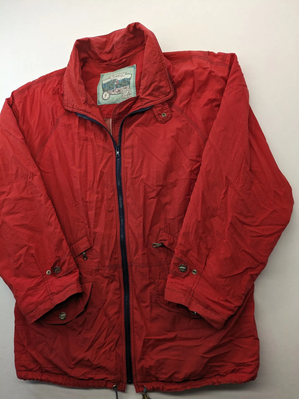 Bush Sportswear red trekking jacket with front zipper, multiple pockets, and striped lining.