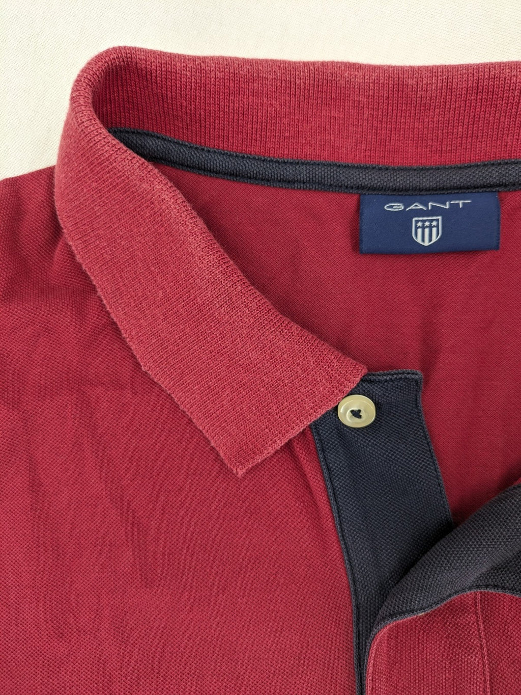 GANT burgundy polo shirt with embroidered shield logo and contrasting navy collar details.