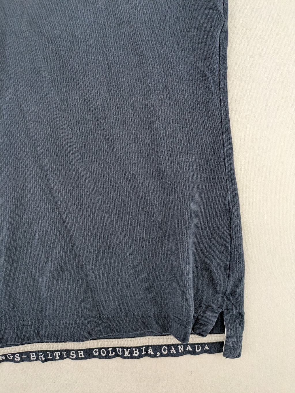 Soccx blue polo shirt with British Columbia graphic, embroidered patches, and striped collar.