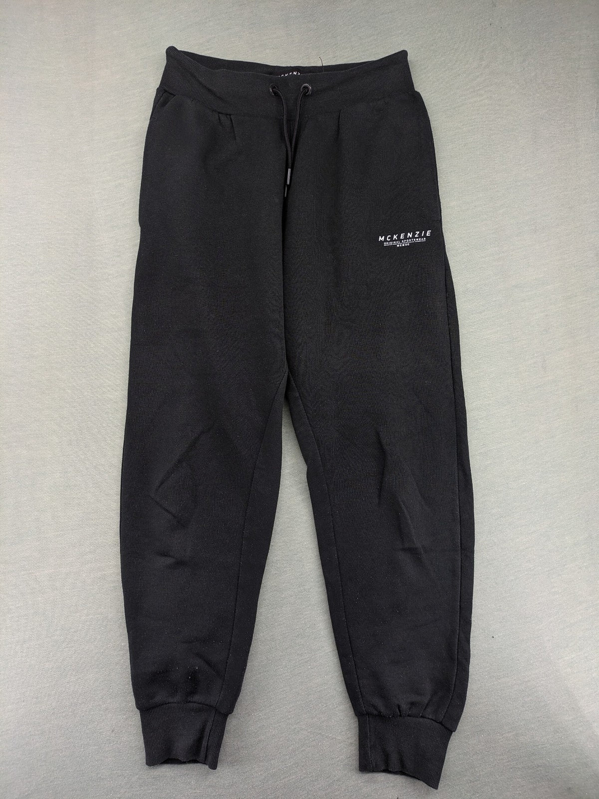 McKenzie black joggers with white logo, tapered fit, and ribbed ankle cuffs.