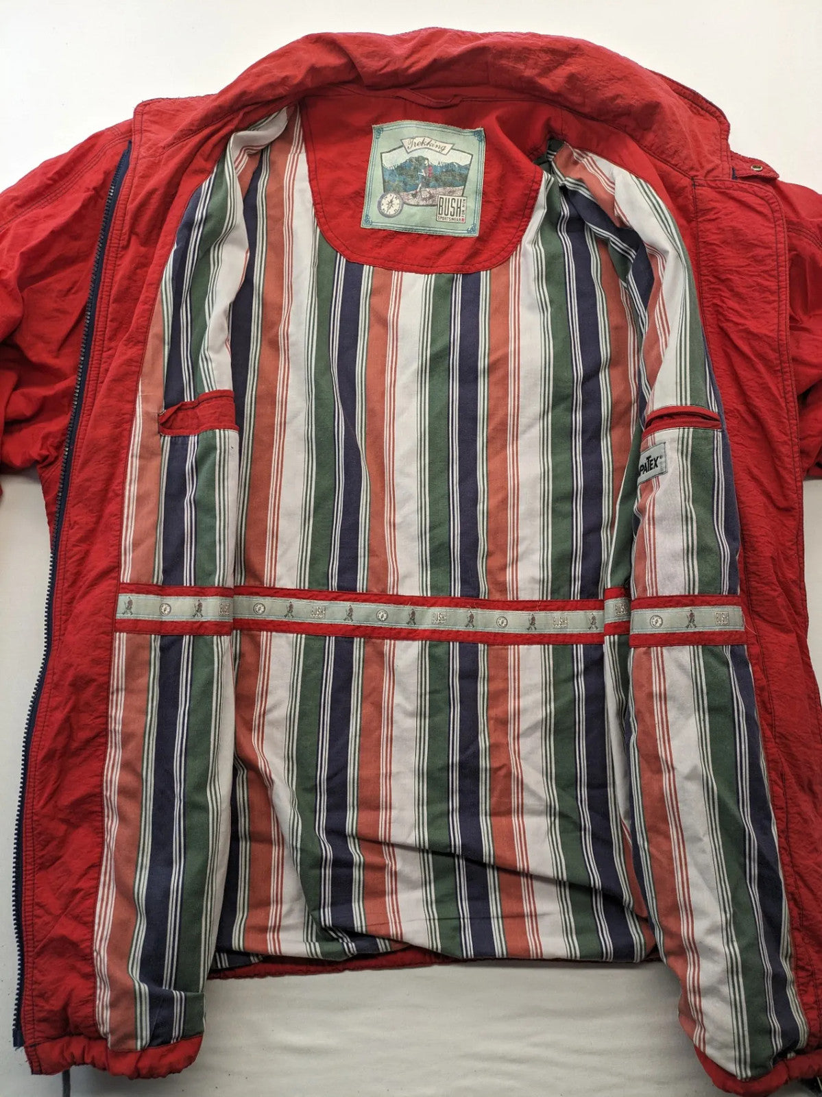 Bush Sportswear red trekking jacket with front zipper, multiple pockets, and striped lining.