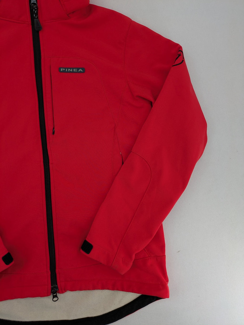 Pinea red softshell jacket with adjustable hood and fleece lining, multiple zippered pockets.
