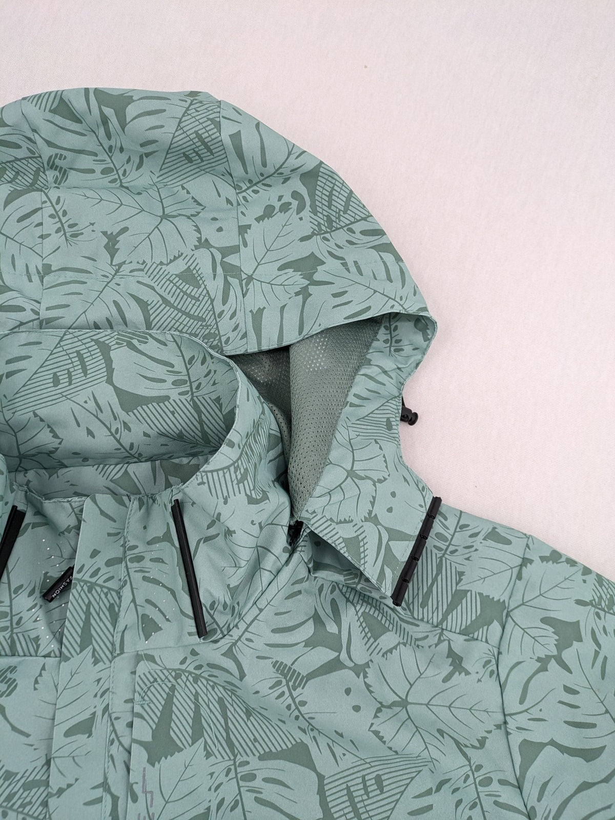 Outdoor green jacket with allover leaf print, adjustable hood, and front zipper.
