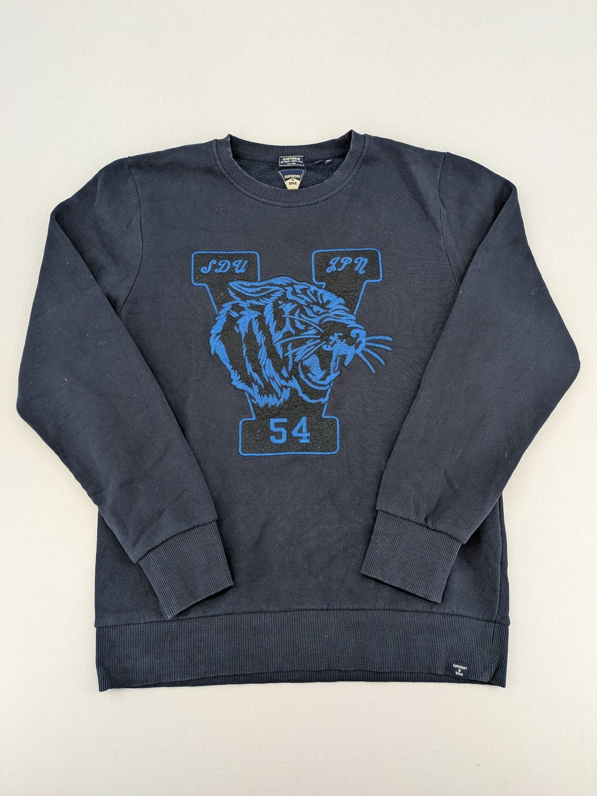 Superdry navy sweatshirt with embroidered tiger graphic and "JPN 54" chenille detail.