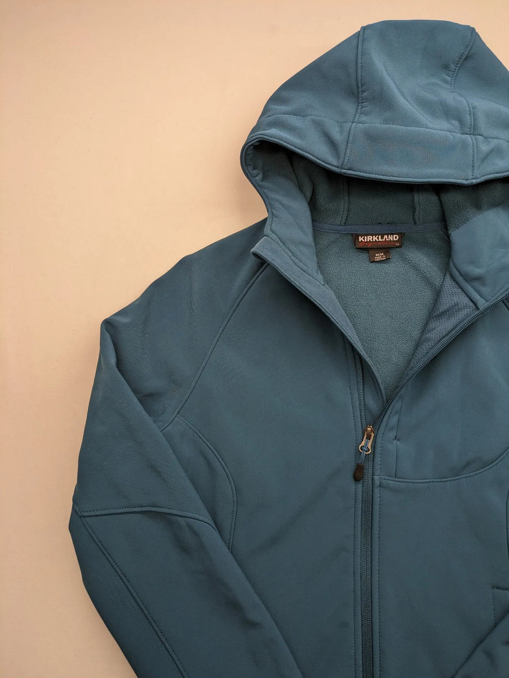 Kirkland Signature blue softshell jacket with hood, fleece lining, and zippered pockets.